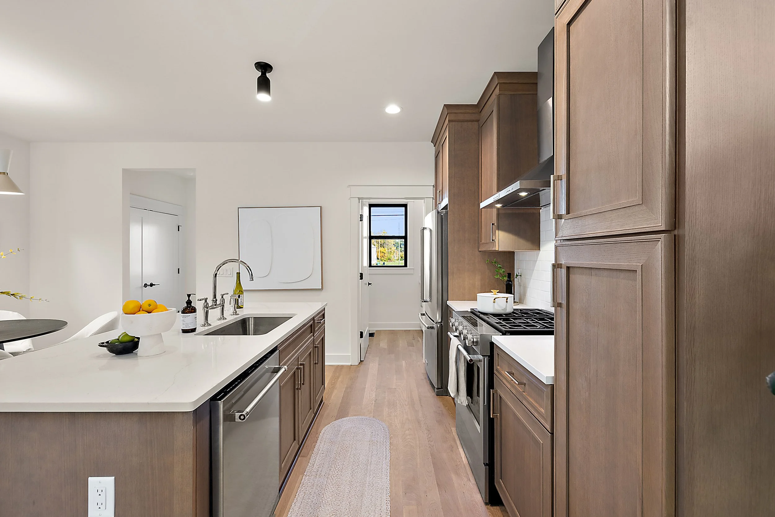 Modern kitchen with wooden cabinets, white countertops, stainless steel appliances, a small window, and minimalist decor.