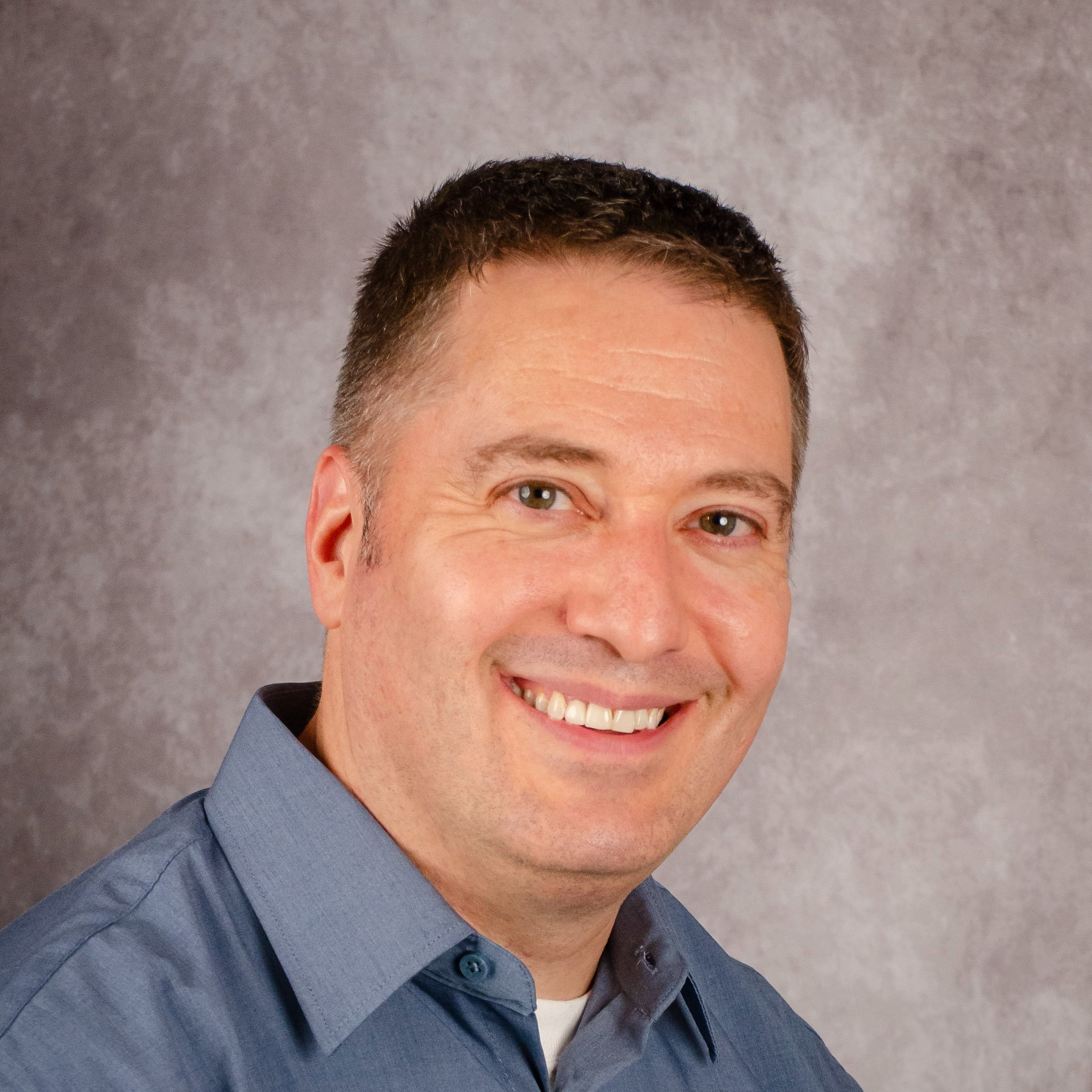 Man smiling in a blue shirt against a gray background.