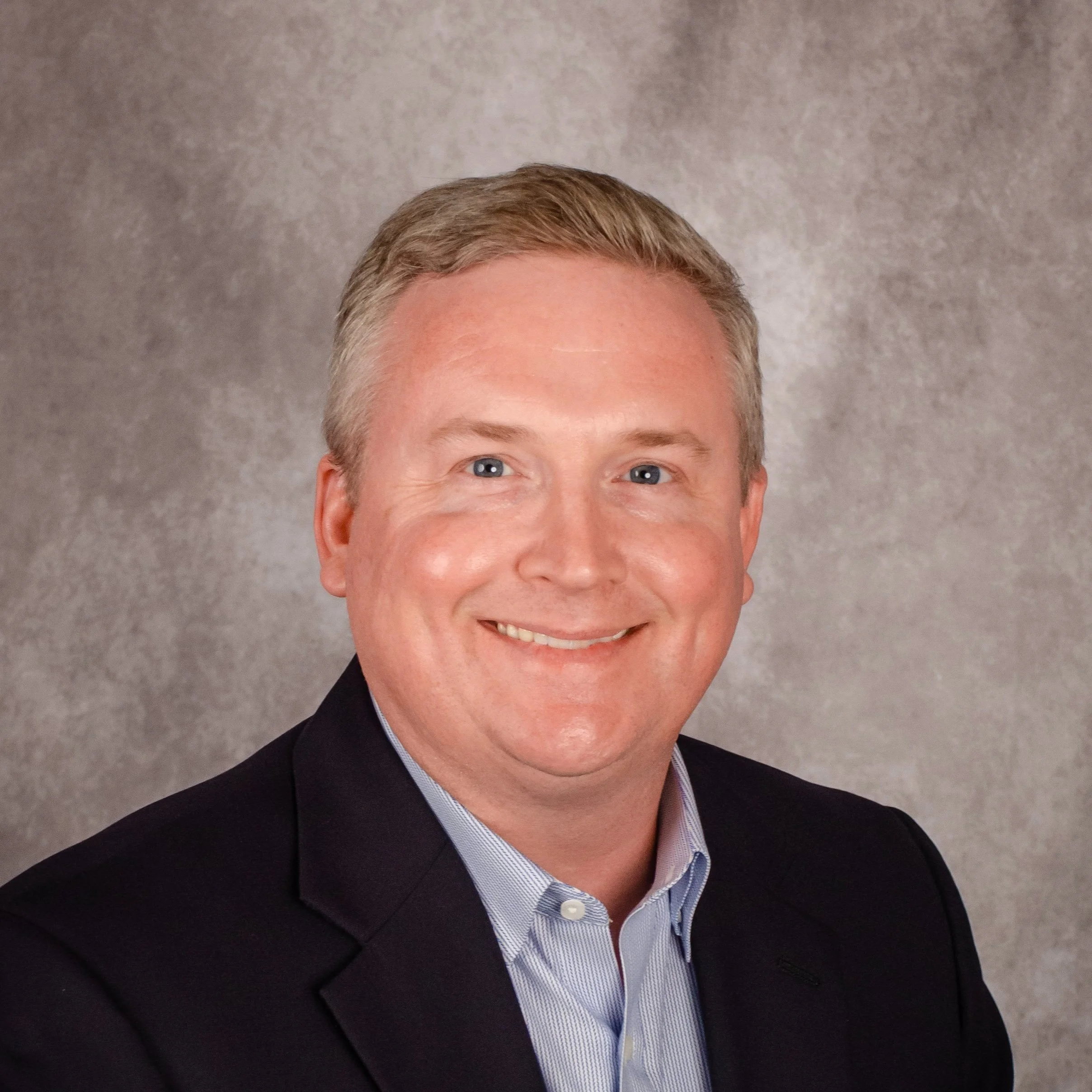 Smiling man in a suit with a gray background.