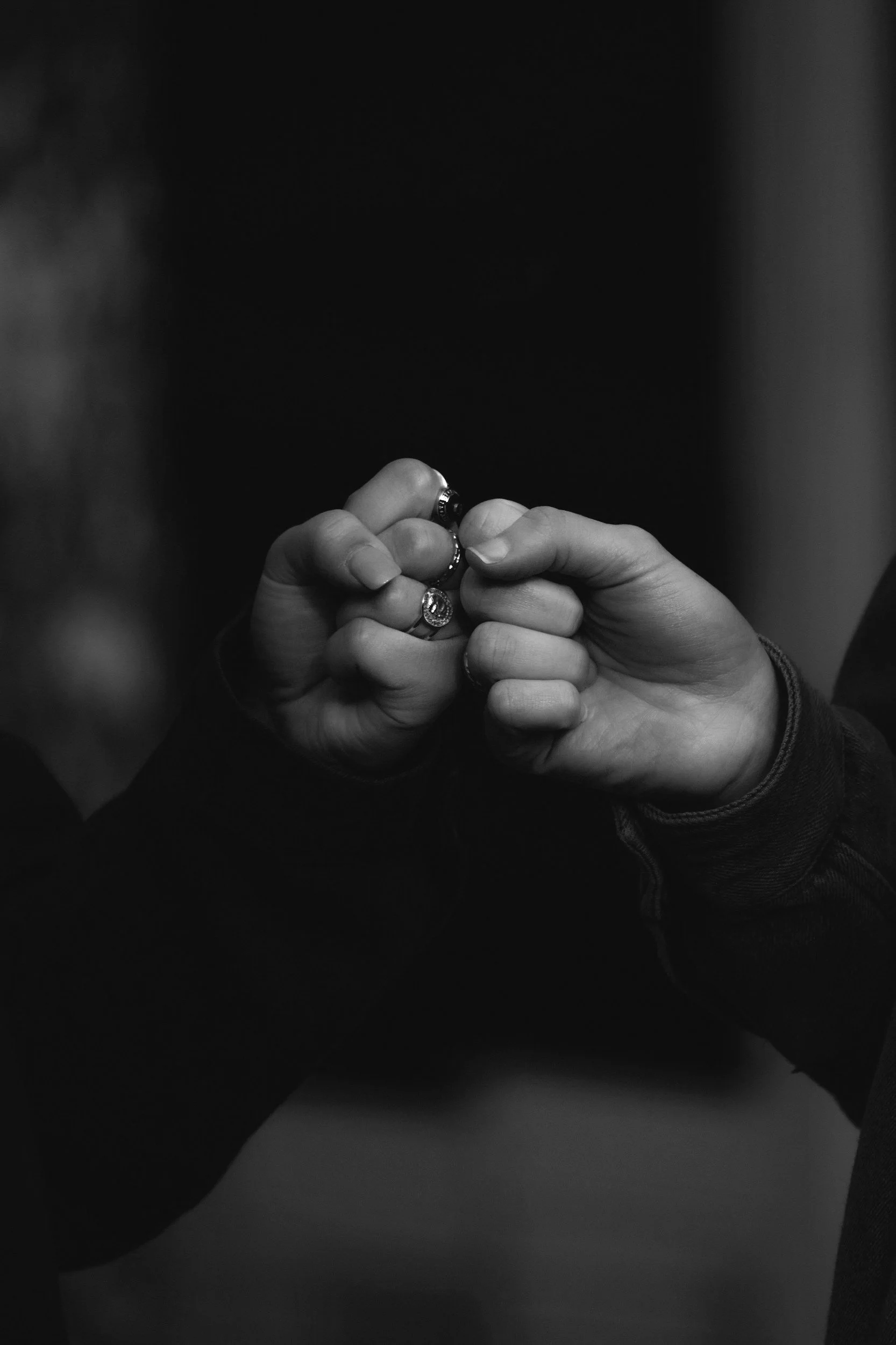 Two hands with rings clasped together in a fist bump, black and white photograph.