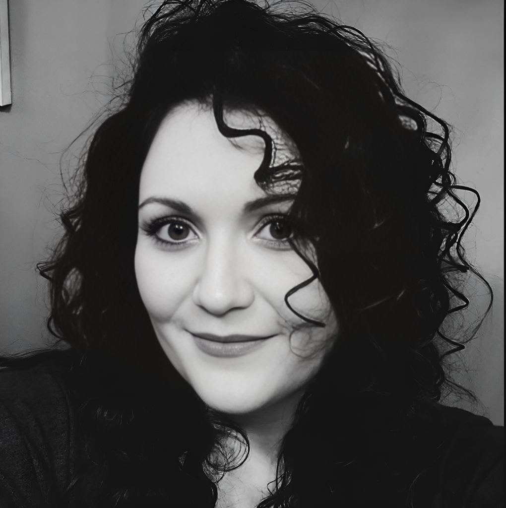 Black and white close-up photo of a woman with curly hair, smiling at the camera.