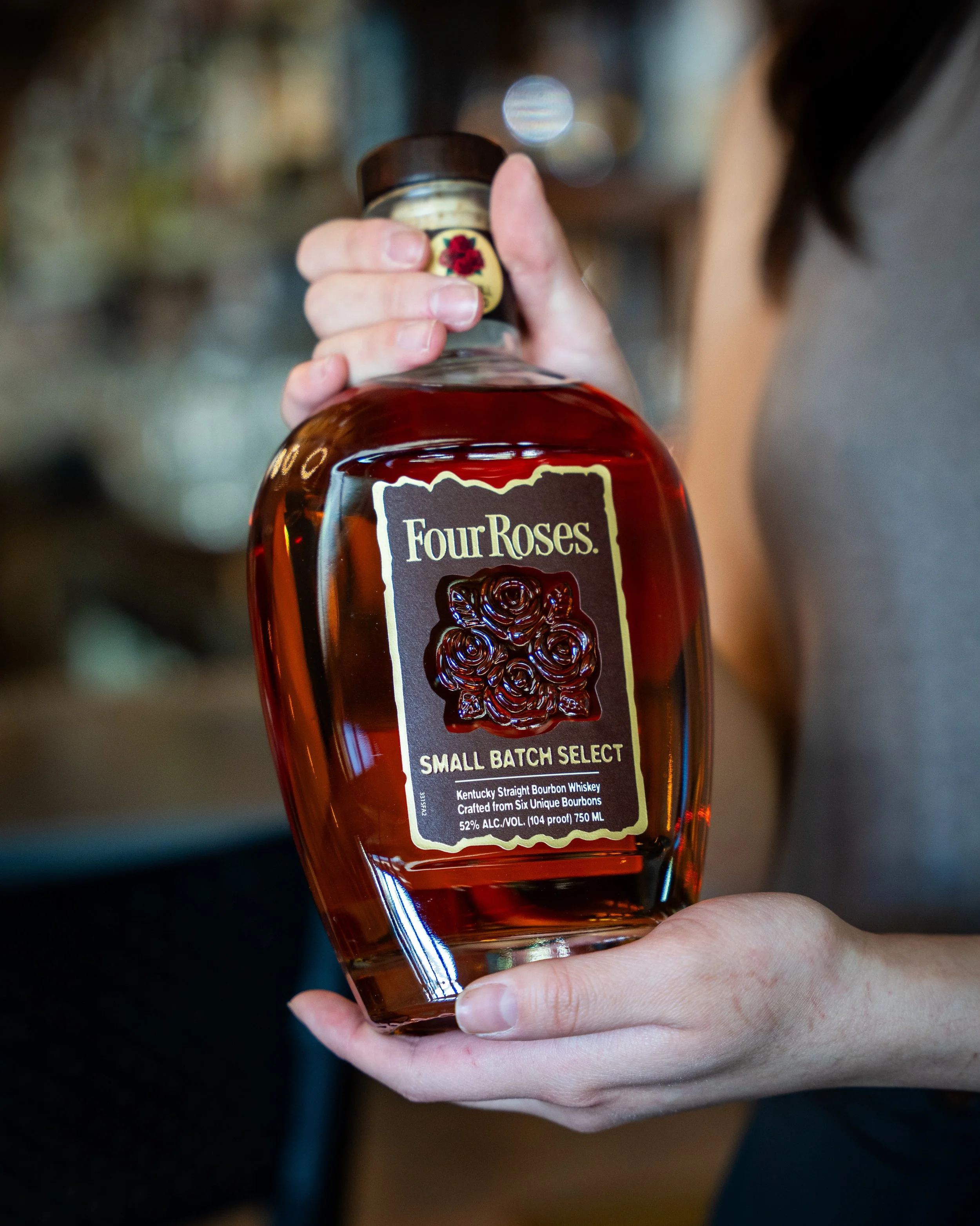 A person holding a bottle of Four Roses small batch select bourbon whiskey.