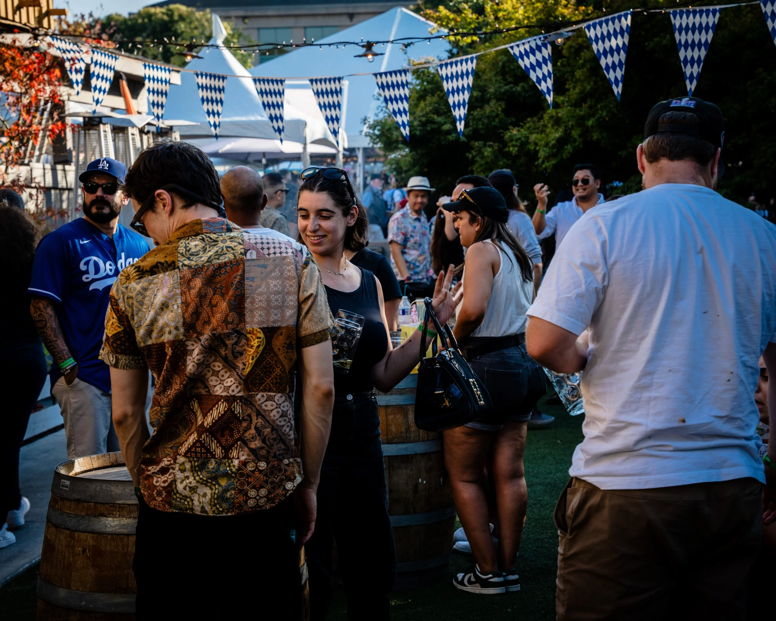 People gathering at an outdoor event with blue and white checkered banners, some holding drinks and socializing.