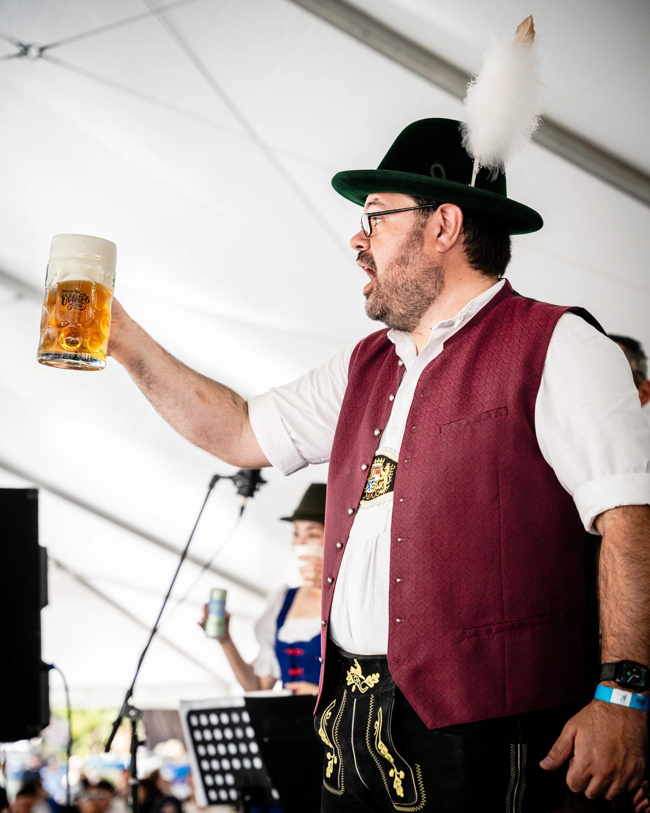 Man dressed in traditional Bavarian attire holding a beer mug at a festival