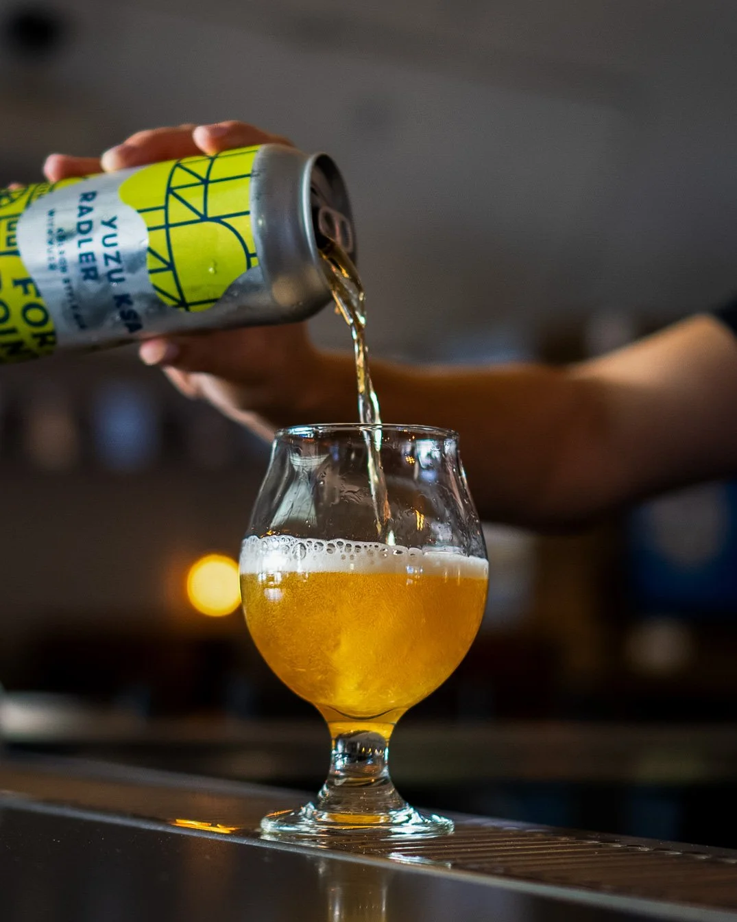 Someone pours a can of Yuzu Radler into a glass of beer on a bar counter.