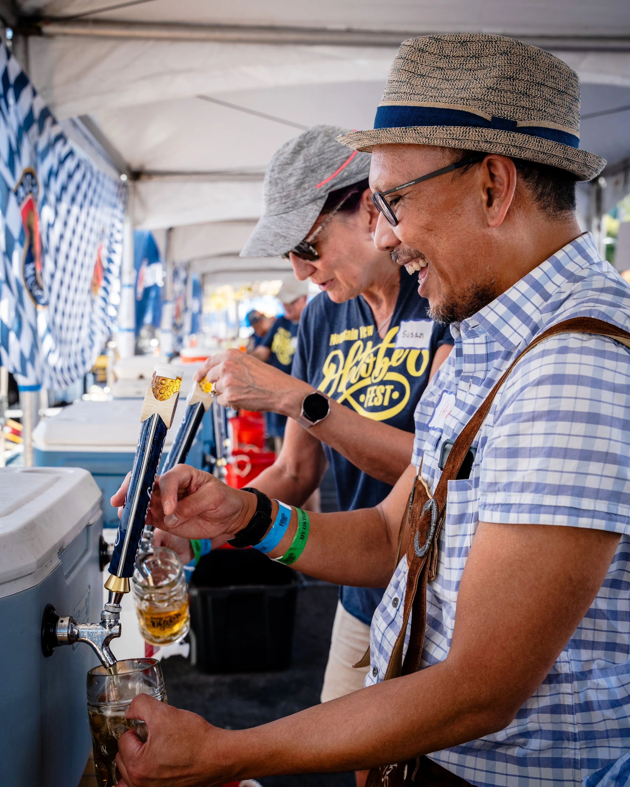 People at a festival pouring beer from taps into glasses under a tent.