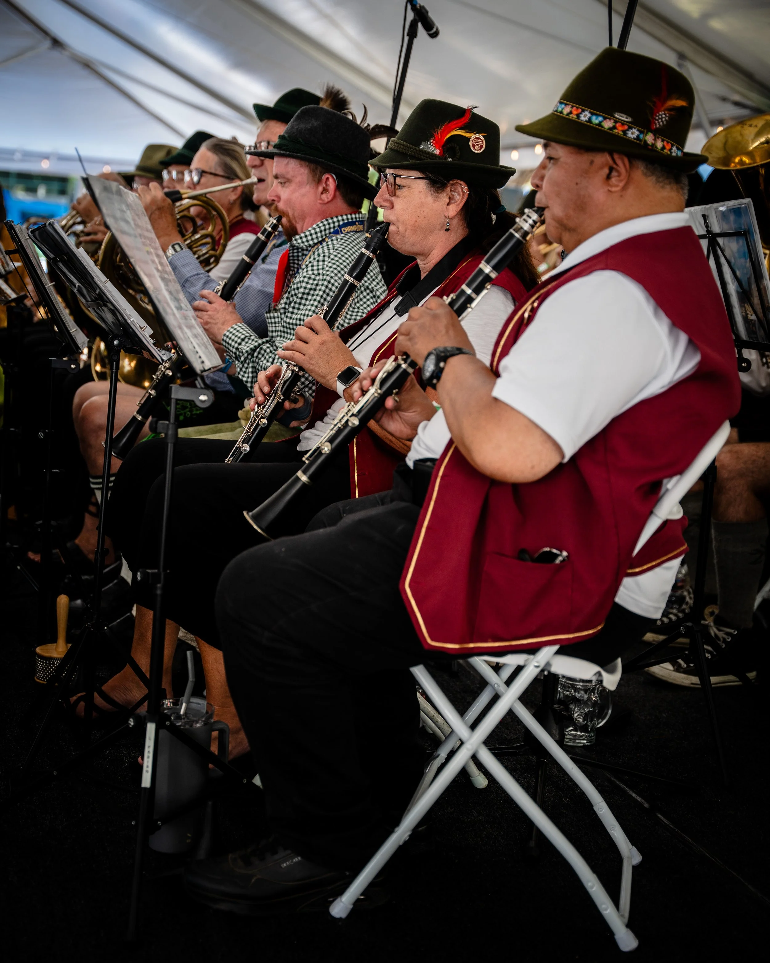 Group of musicians in traditional Bavarian attire playing wind instruments at an indoor event.