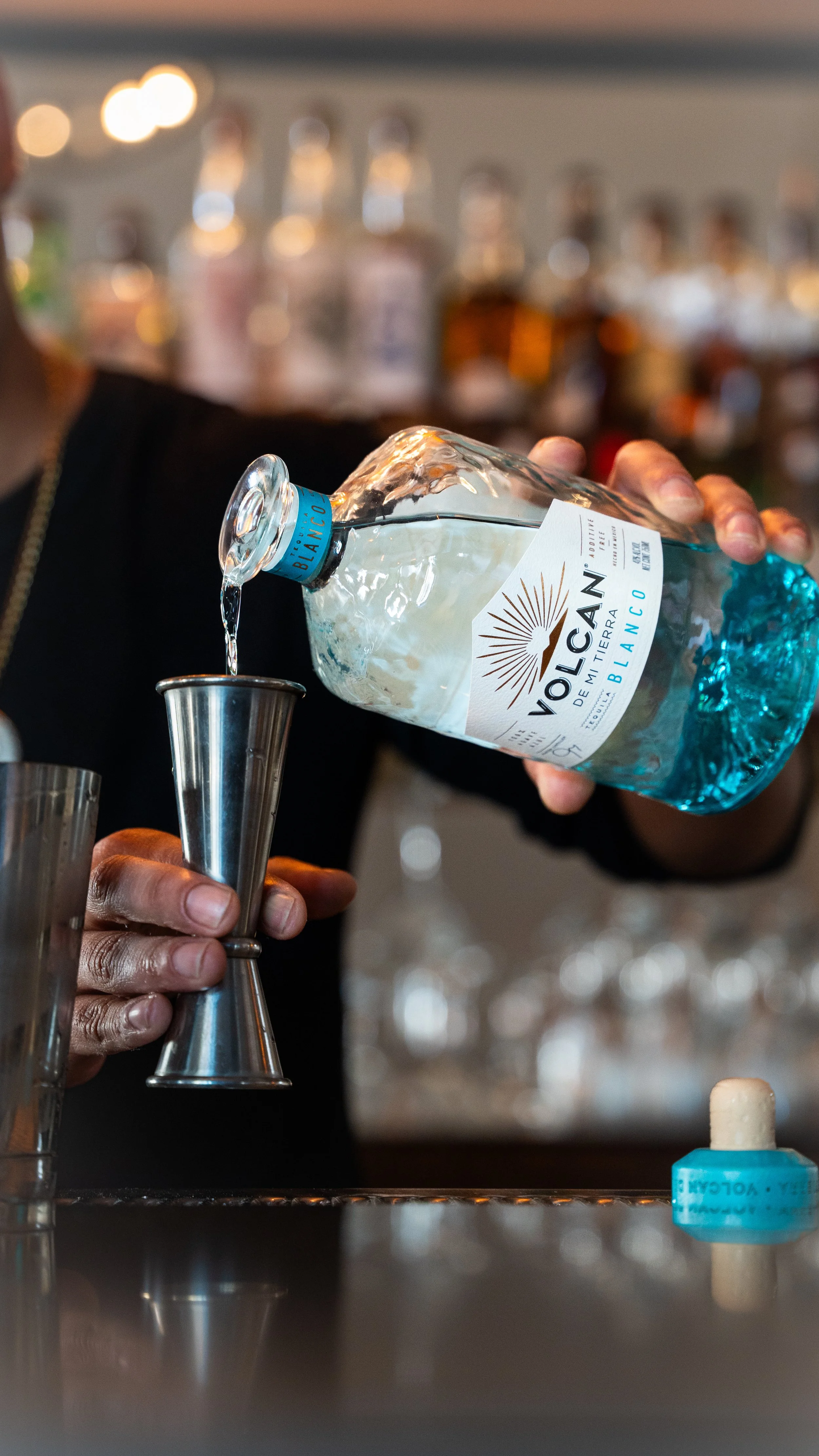 Person pouring mineral water from a Vatican labeled bottle into a jigger at a bar.