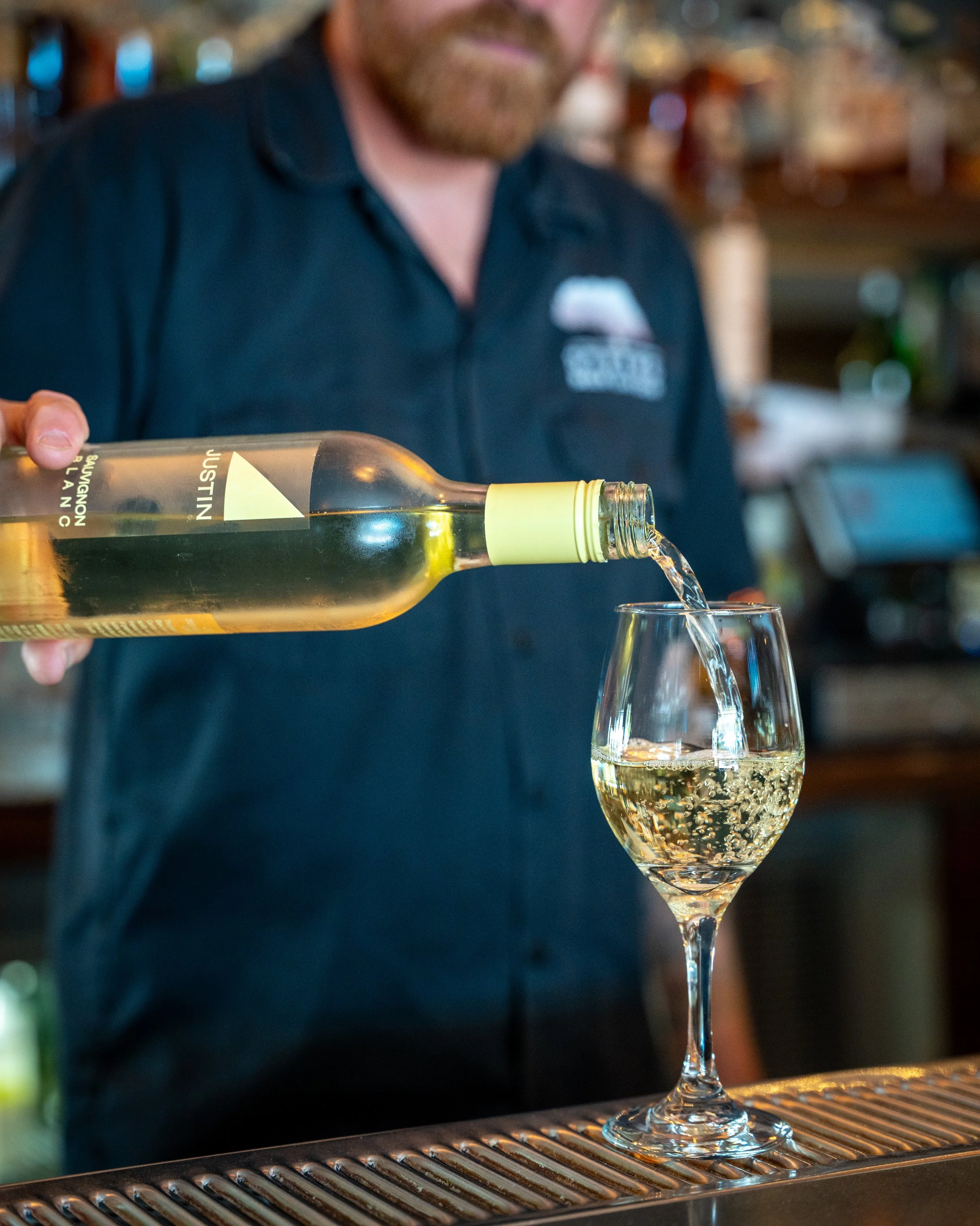 A bartender is pouring white wine into a glass at a bar.