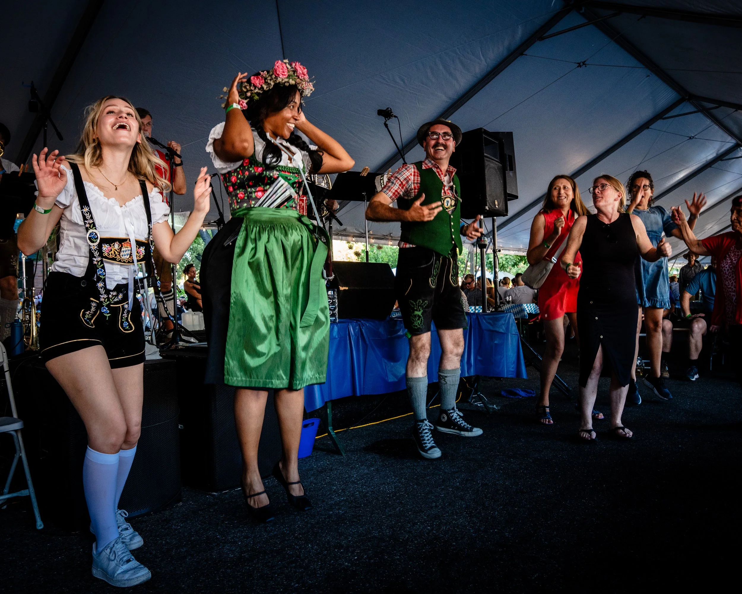 People enjoying traditional Bavarian attire and dancing at an indoor festival under a large tent.
