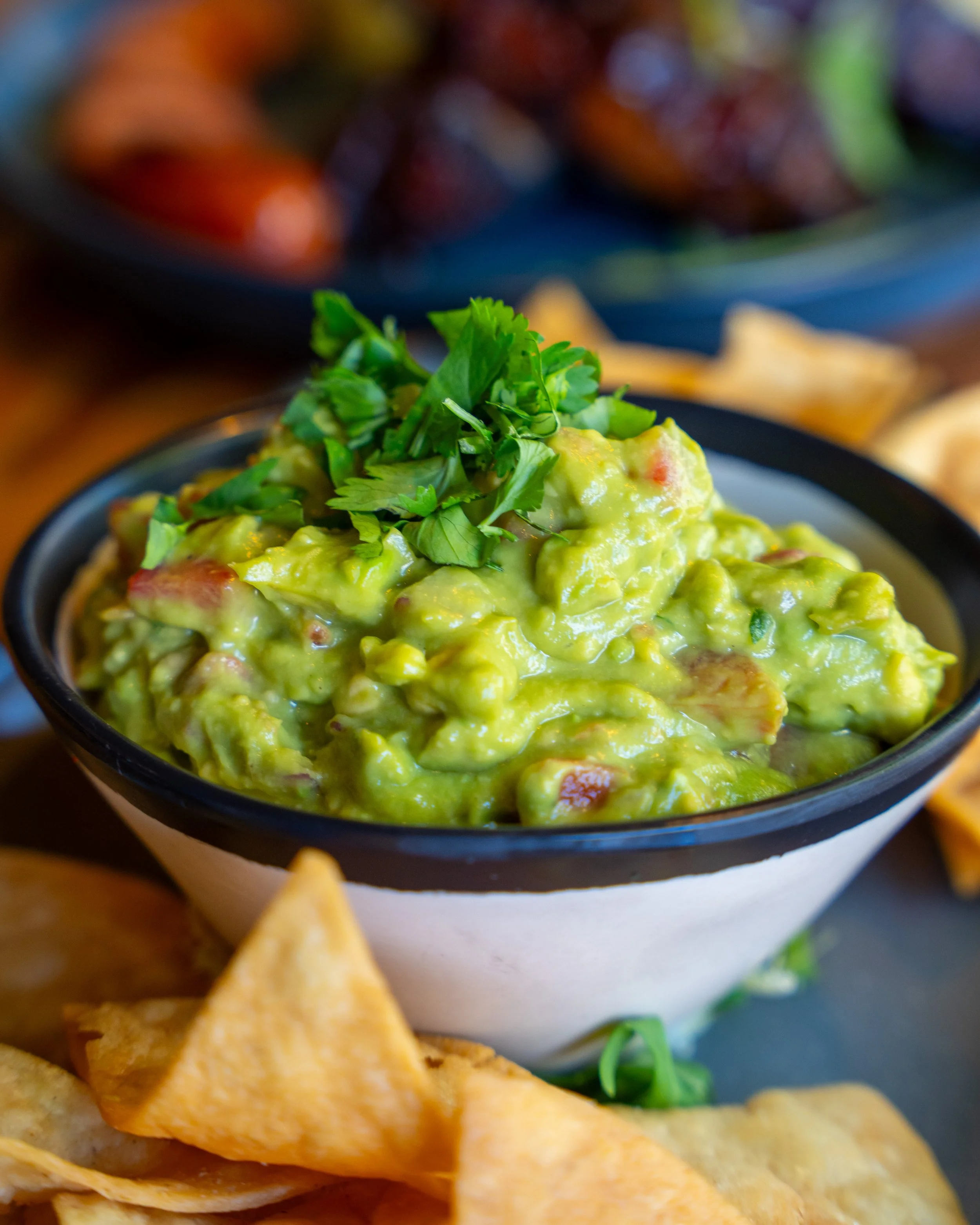 Bowl of guacamole garnished with cilantro and surrounded by tortilla chips.