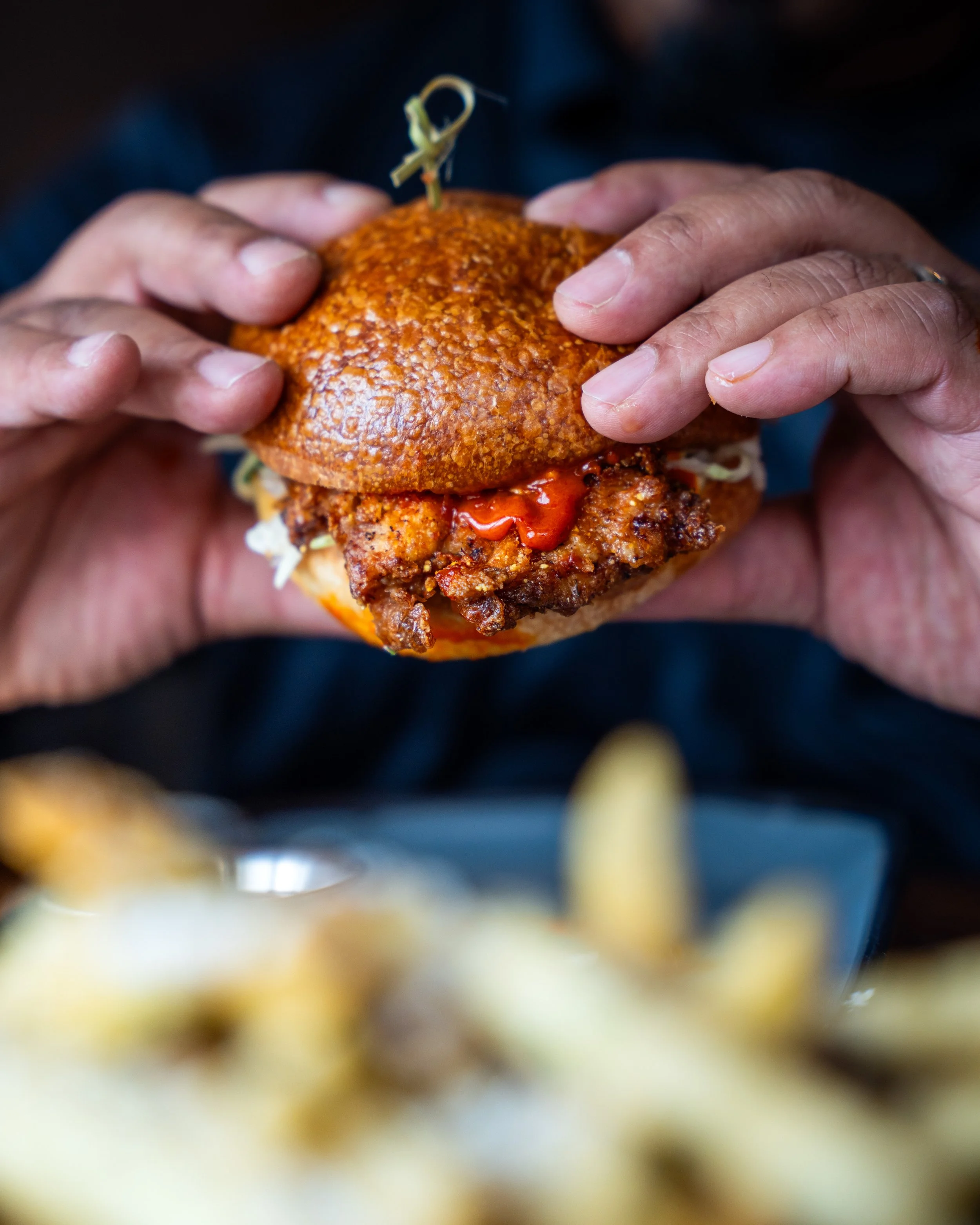 Person holding a burger with fried chicken patty, lettuce, and ketchup in a bun