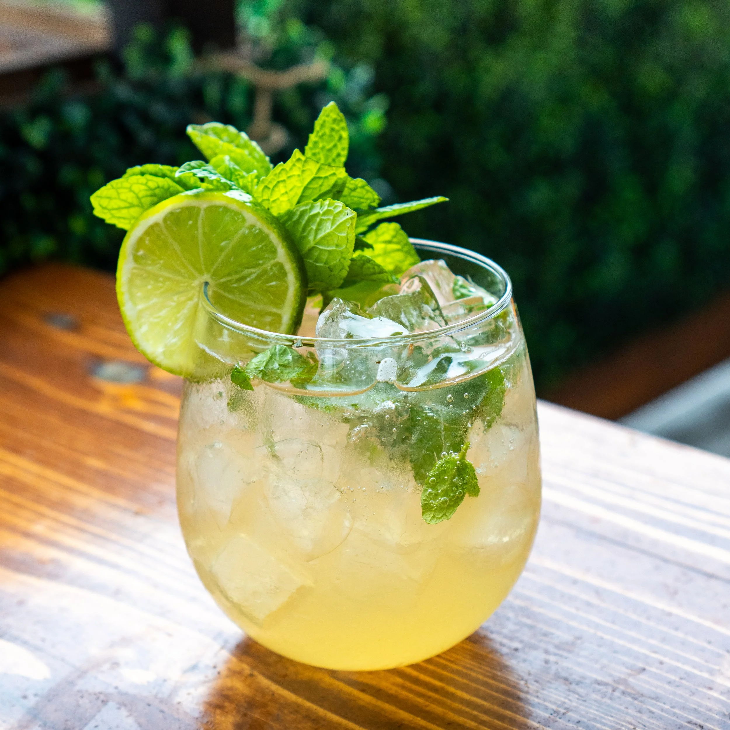 A glass of lemonade cocktail garnished with a slice of lime and sprigs of mint, with ice cubes inside.
