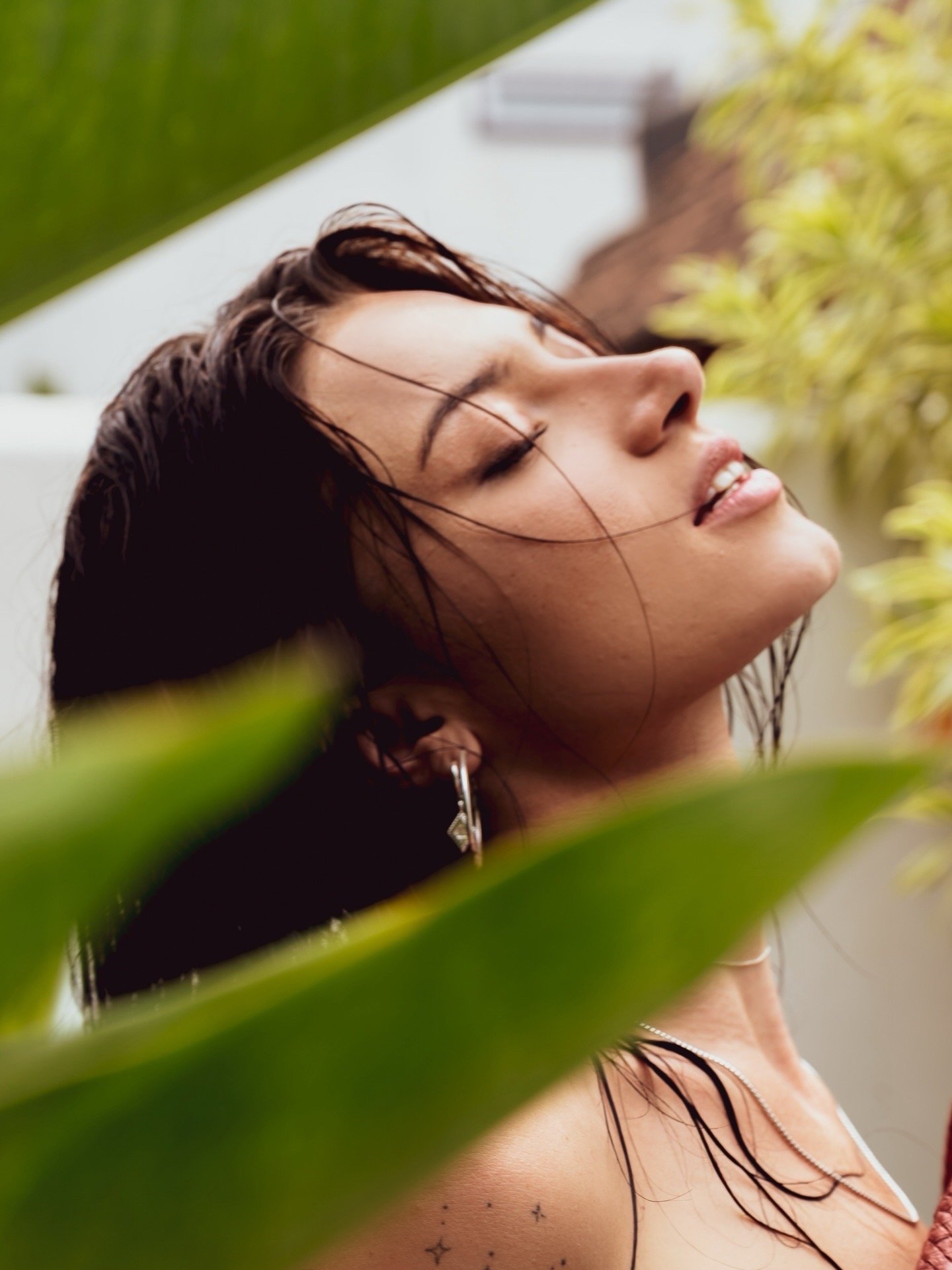 A woman with wet hair and earrings enjoying the outdoors with her eyes closed and a peaceful expression.