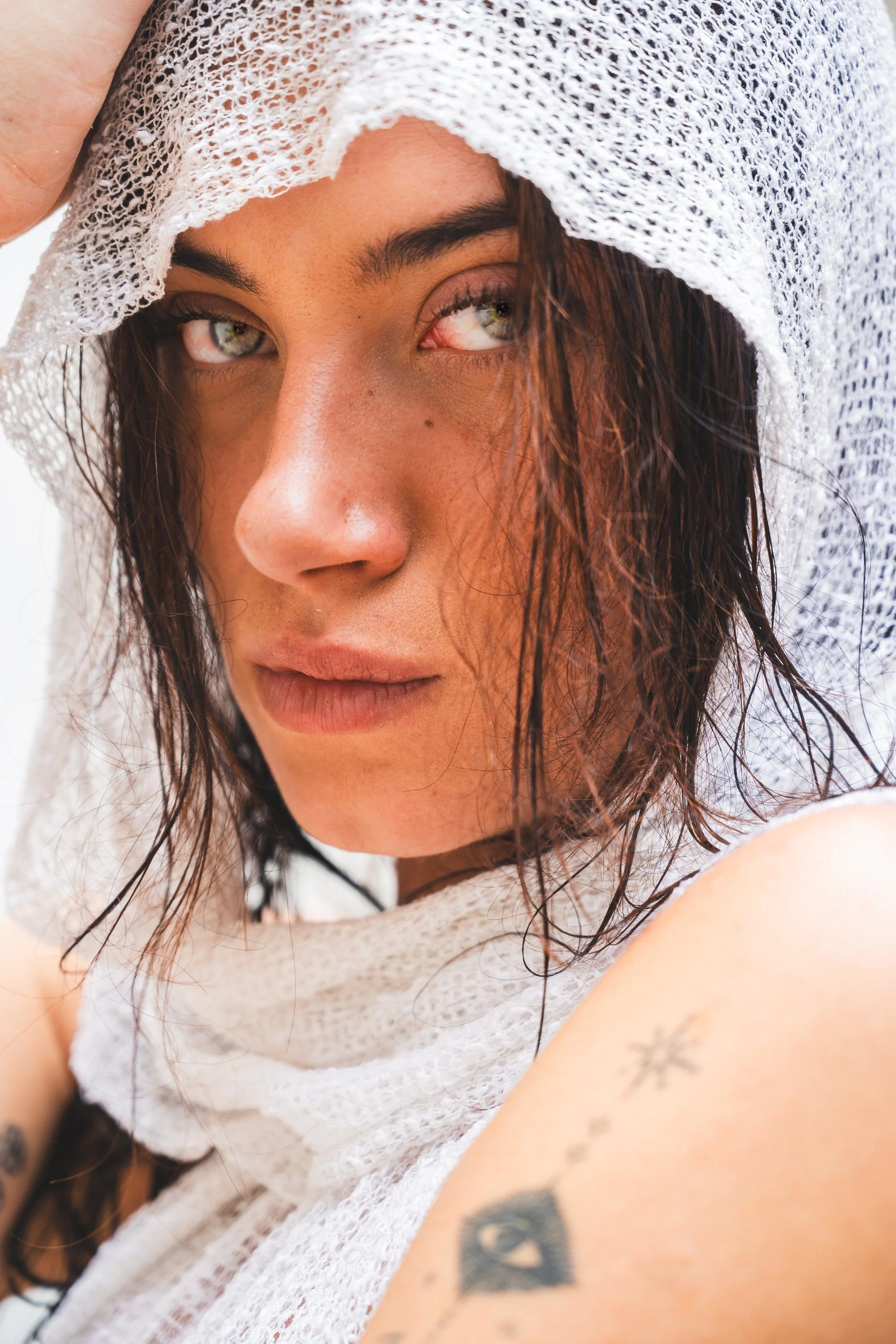 Close-up of a woman with wet hair wearing a white knitted hood, looking into the camera with a confident expression.