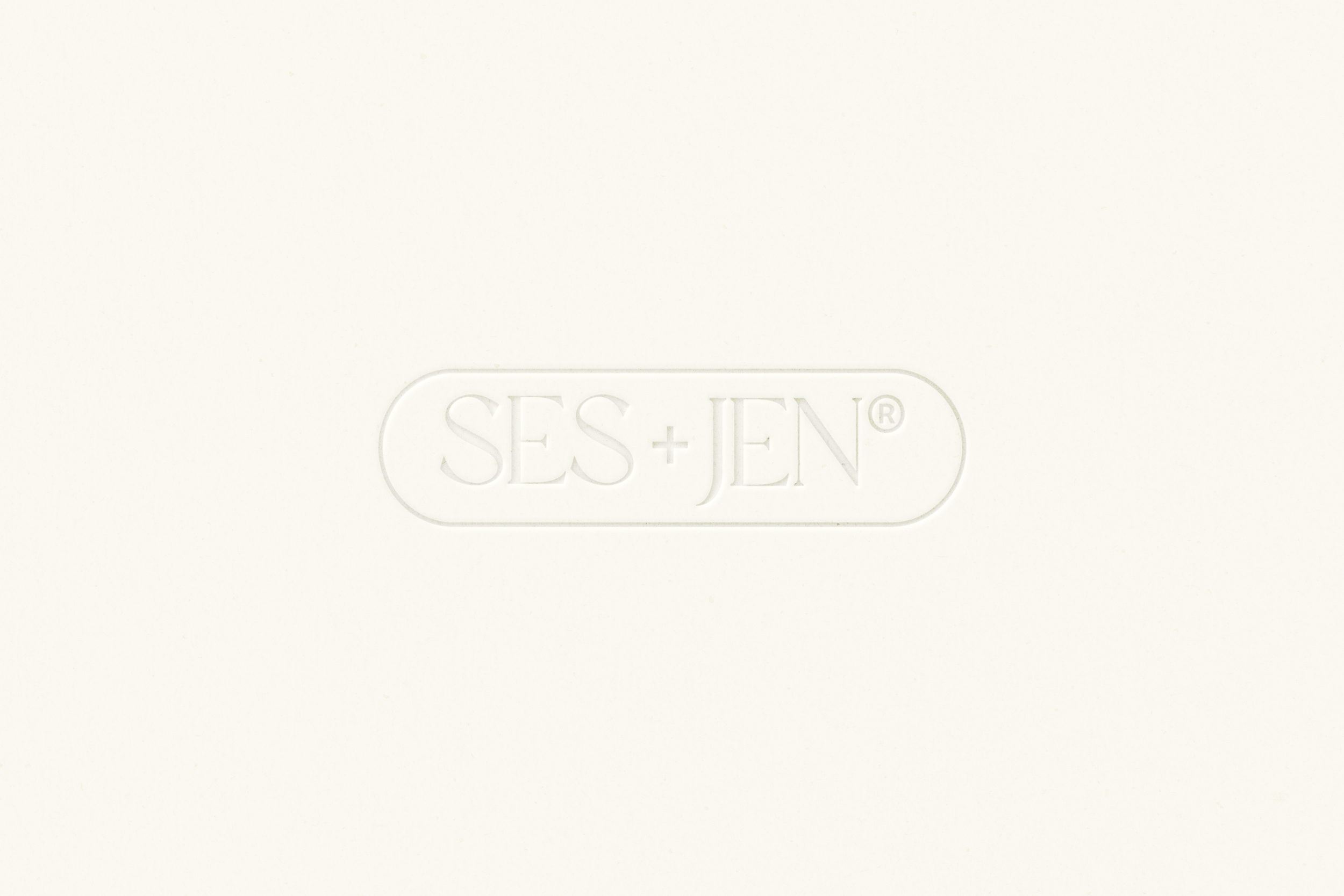 Embossed logo of SES+JEN on a white surface.