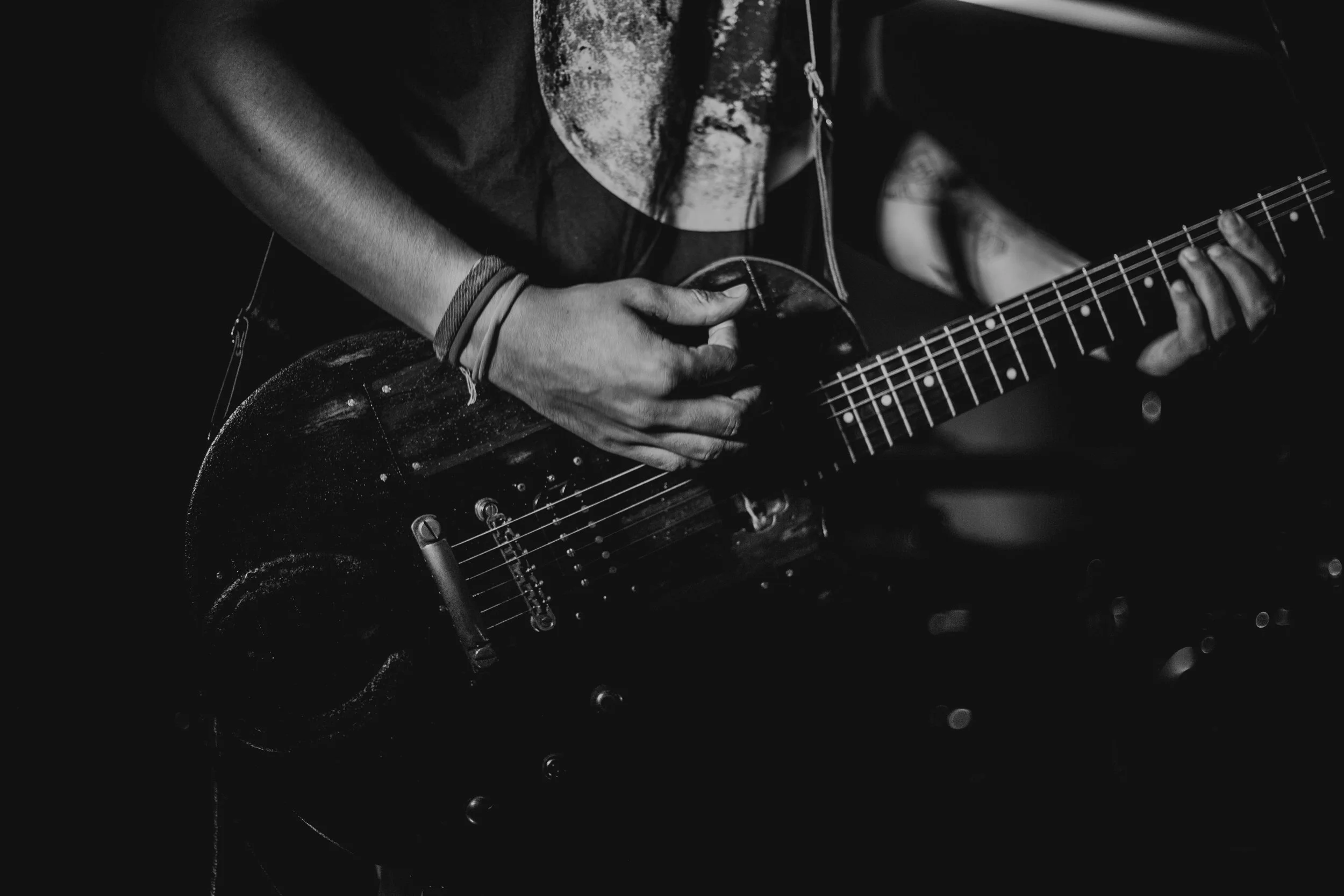 Close-up of a person playing an electric guitar in black and white, focusing on their hands and the guitar.