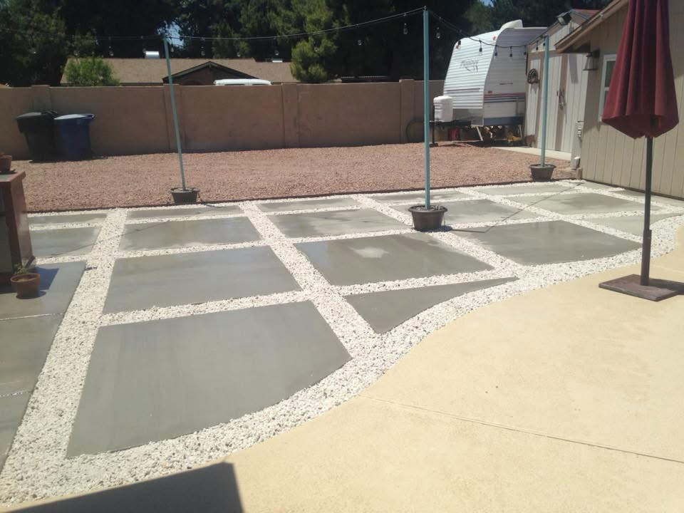 Backyard with concrete tiles, gravel in between, potted plants, a trailer home, and a parasol.