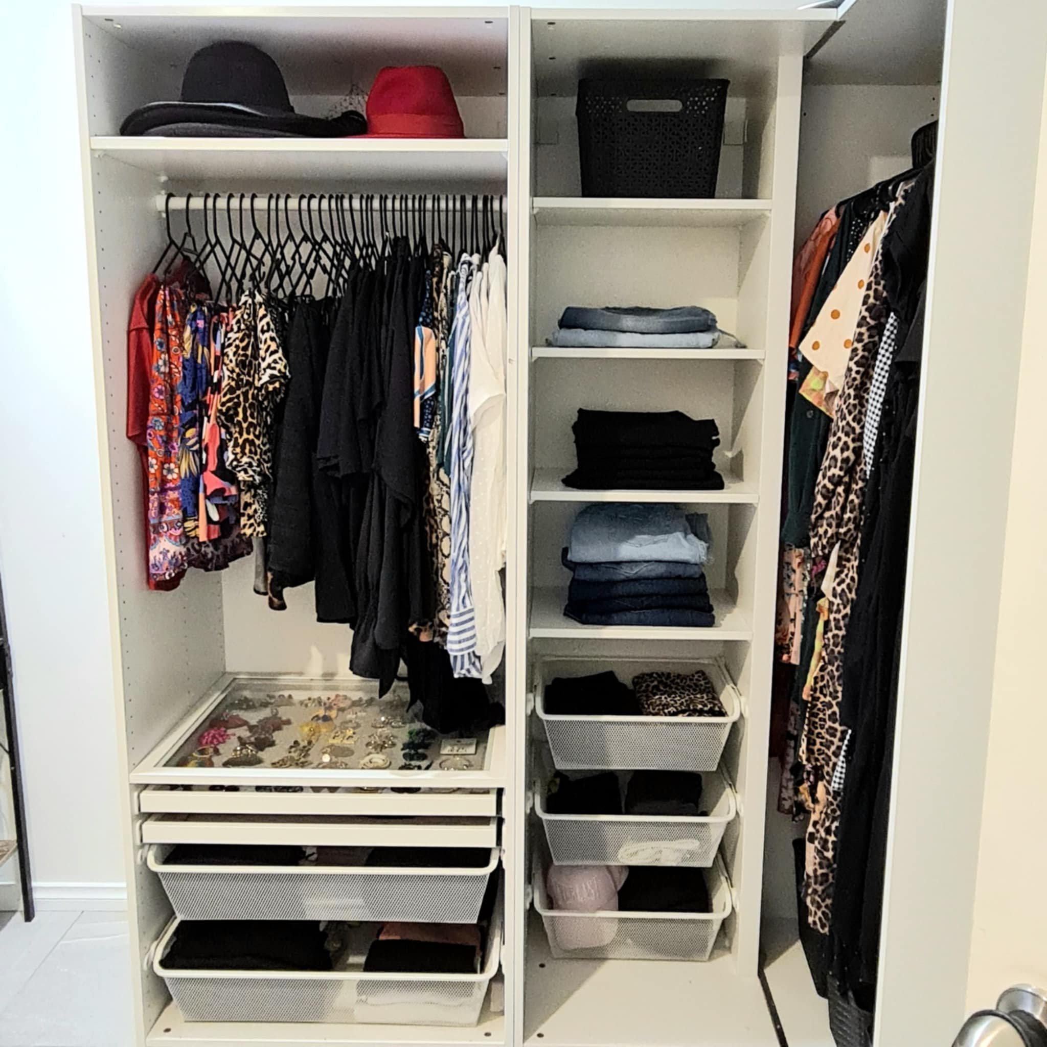 Organized wardrobe with hanging clothes, folded jeans, hats, drawers, and jewelry.