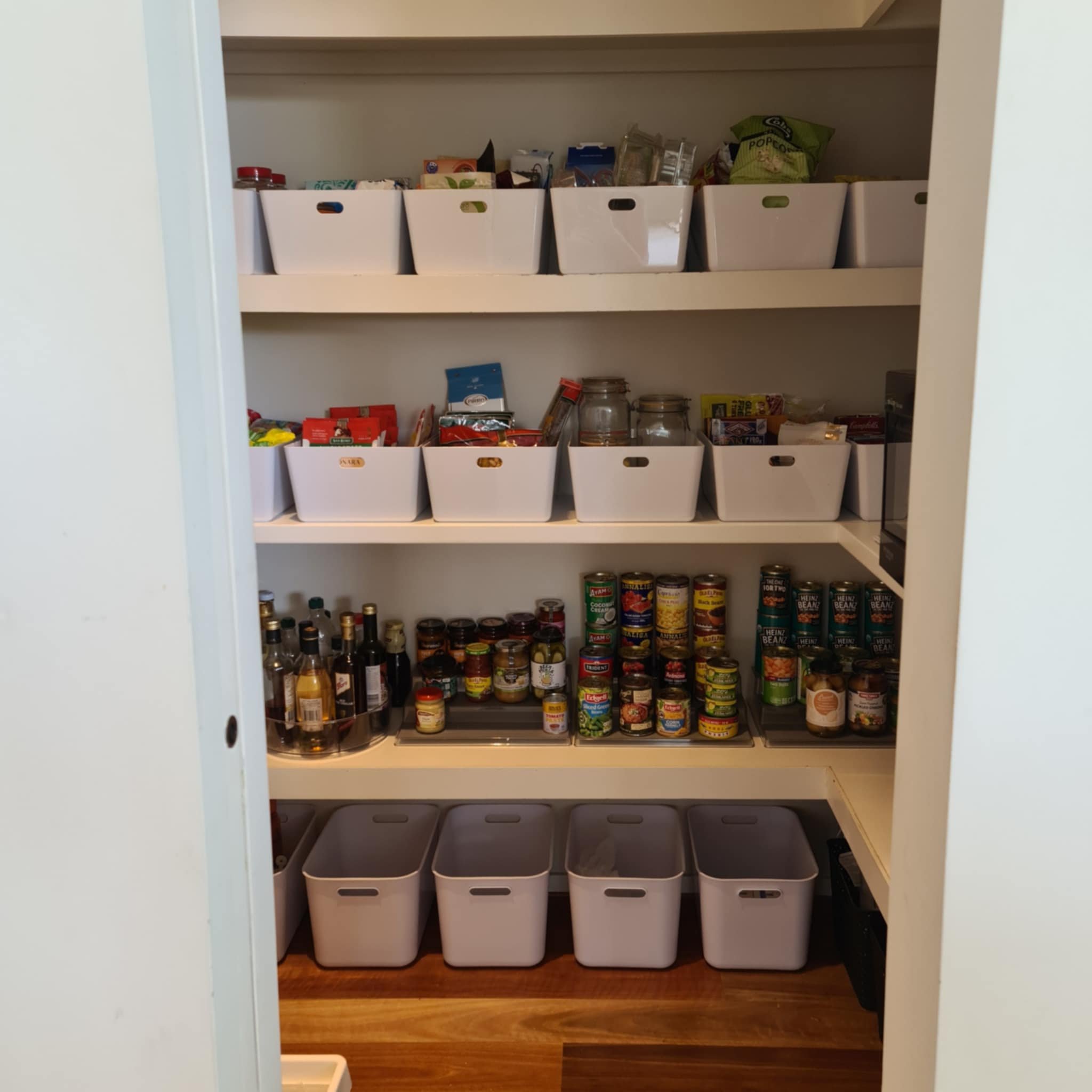 Organized pantry with white storage bins, jars, cans, and bottles on shelves.