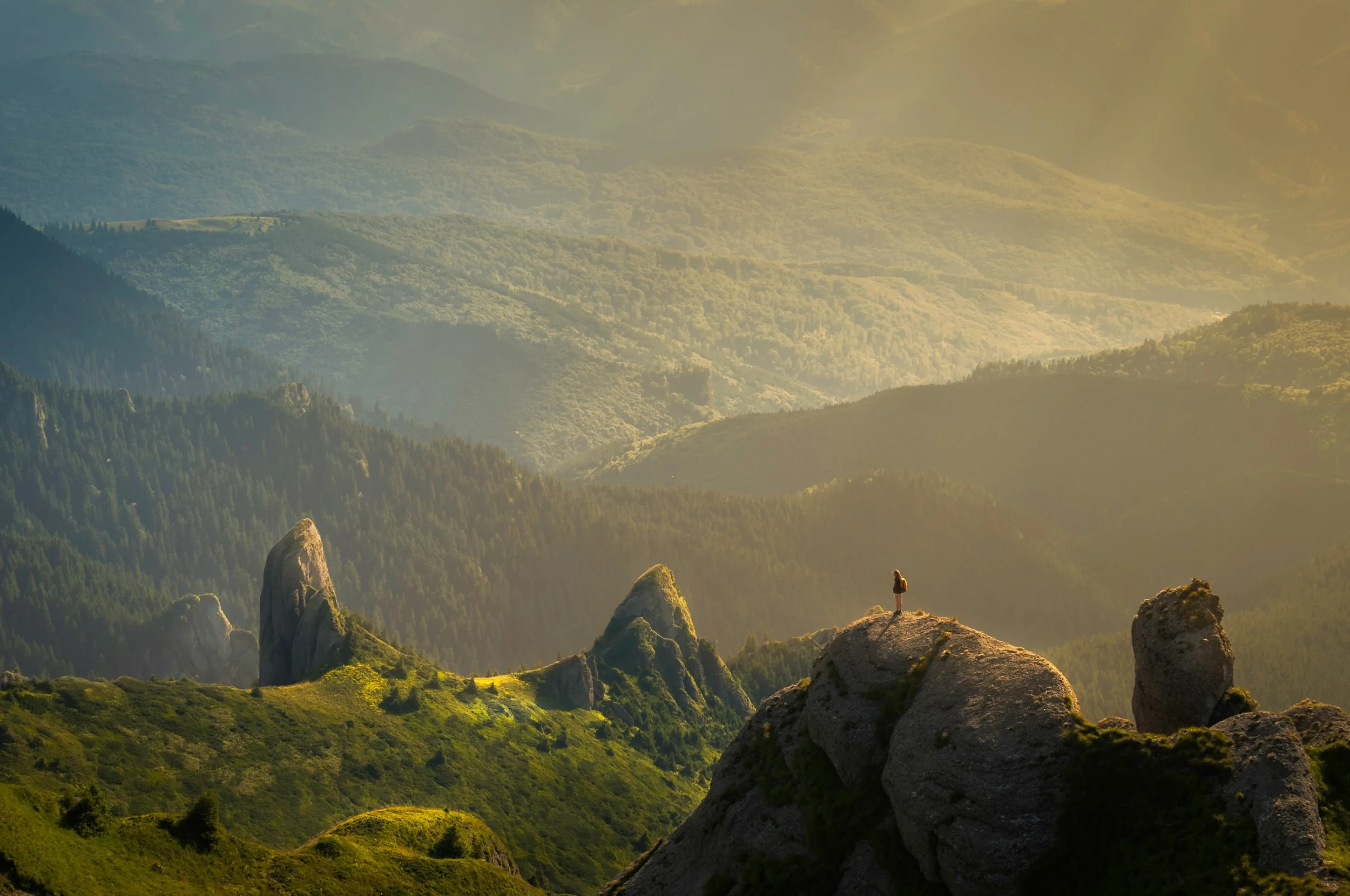 Silhouetted hiker standing on a rock ledge overlooking a lush mountain range at sunrise. A symbol of perspective, self-discovery, and the journey of healing through therapy.