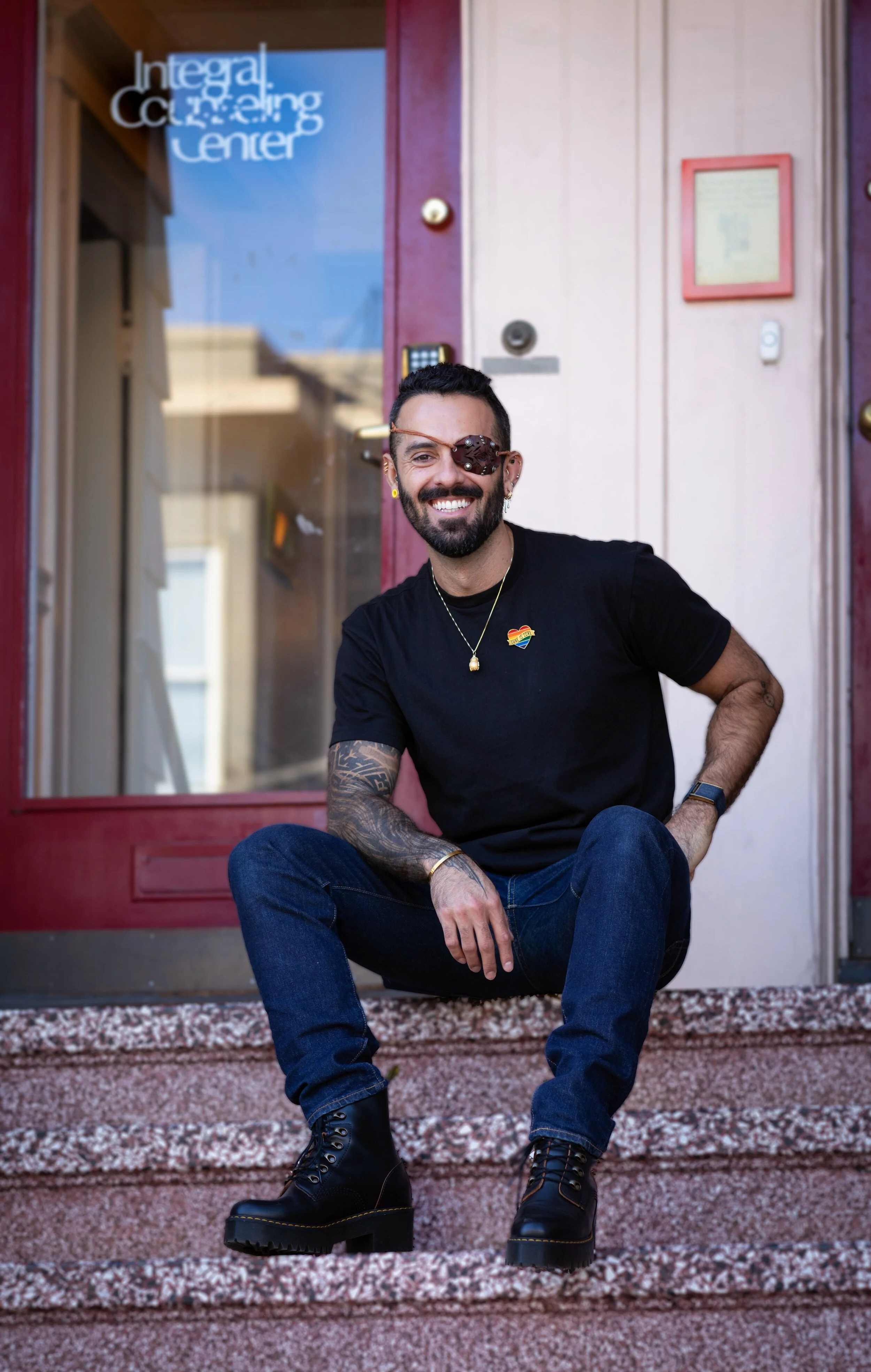 Quest Carrizales (they/them), queer Latinx therapist seated in front of Church Street Integral Counseling Center. Embodied presence, authenticity, and depth in healing.