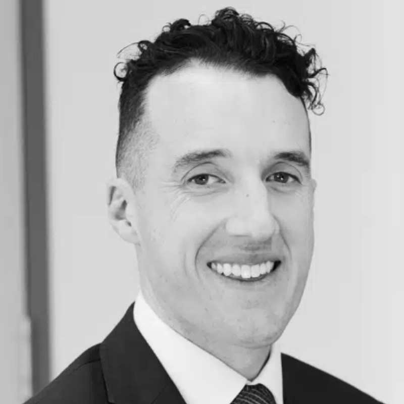 Black and white portrait of a man with short hair, smiling, wearing a suit and tie