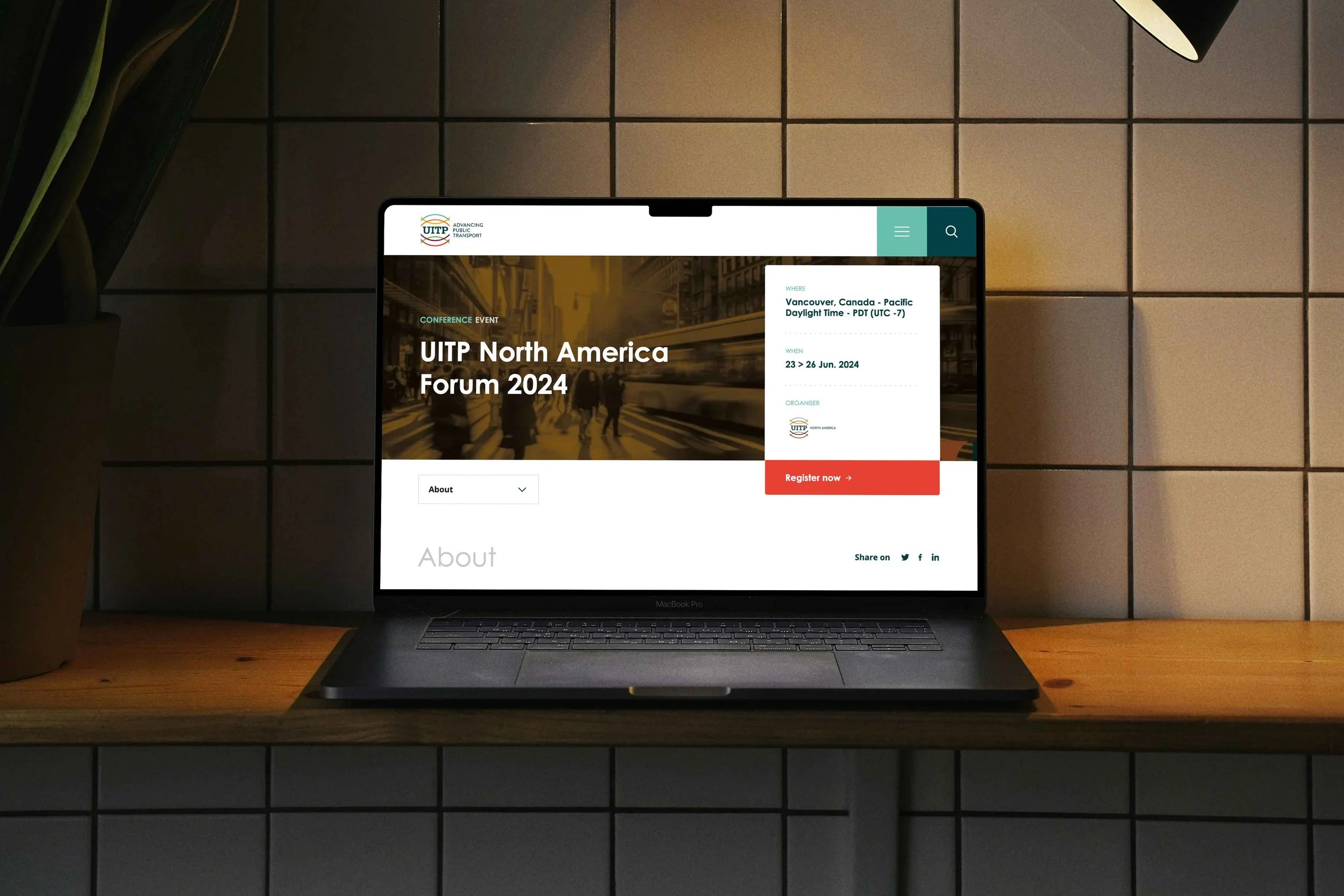 Laptop on a wooden table displaying a website for UITP North America Forum 2024, with event details and registration button, against a tiled wall background.