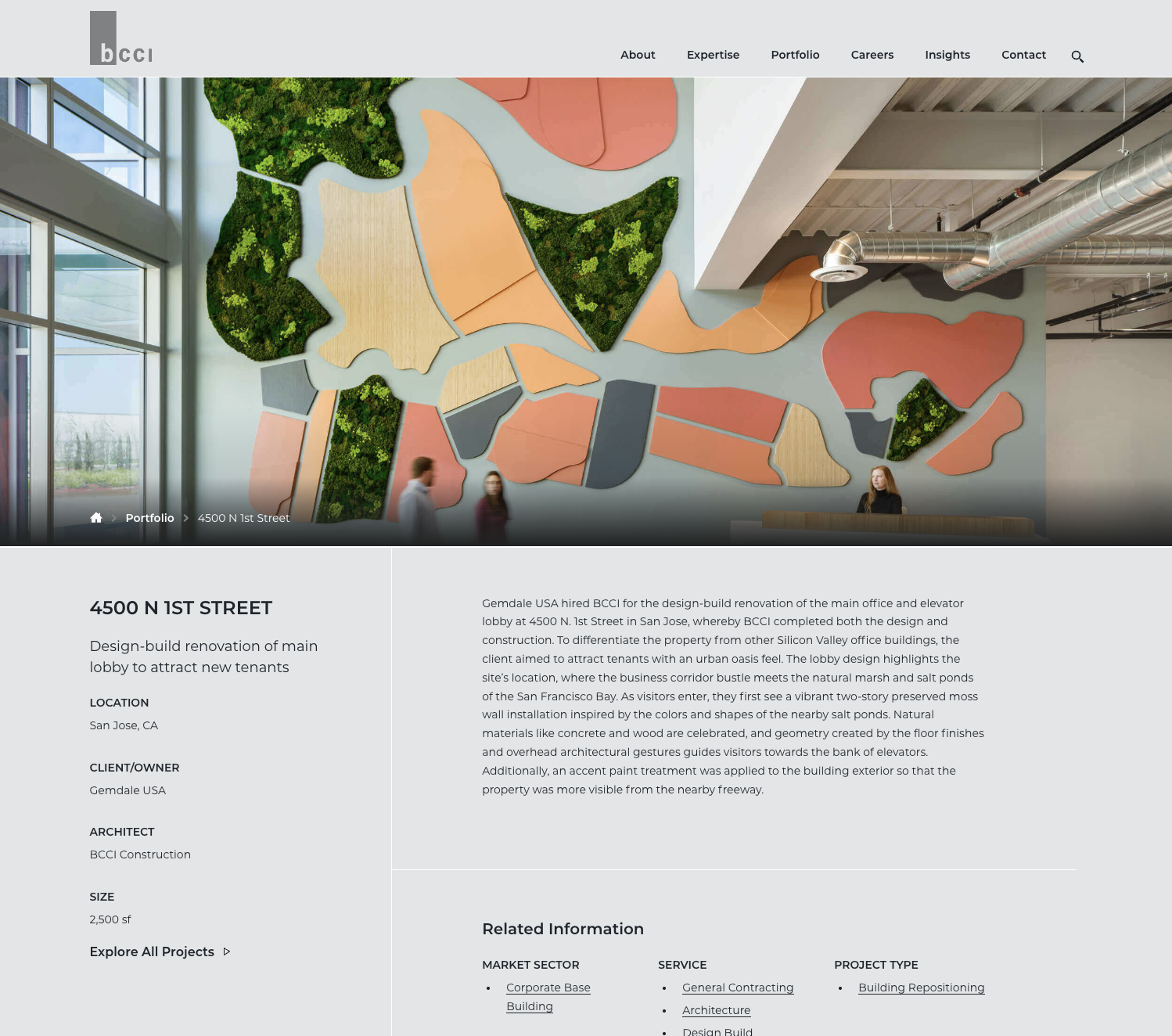 Interior view of a modern office lobby featuring a large abstract wall art installation with colored shapes and green moss accents, a reception desk, and people walking.