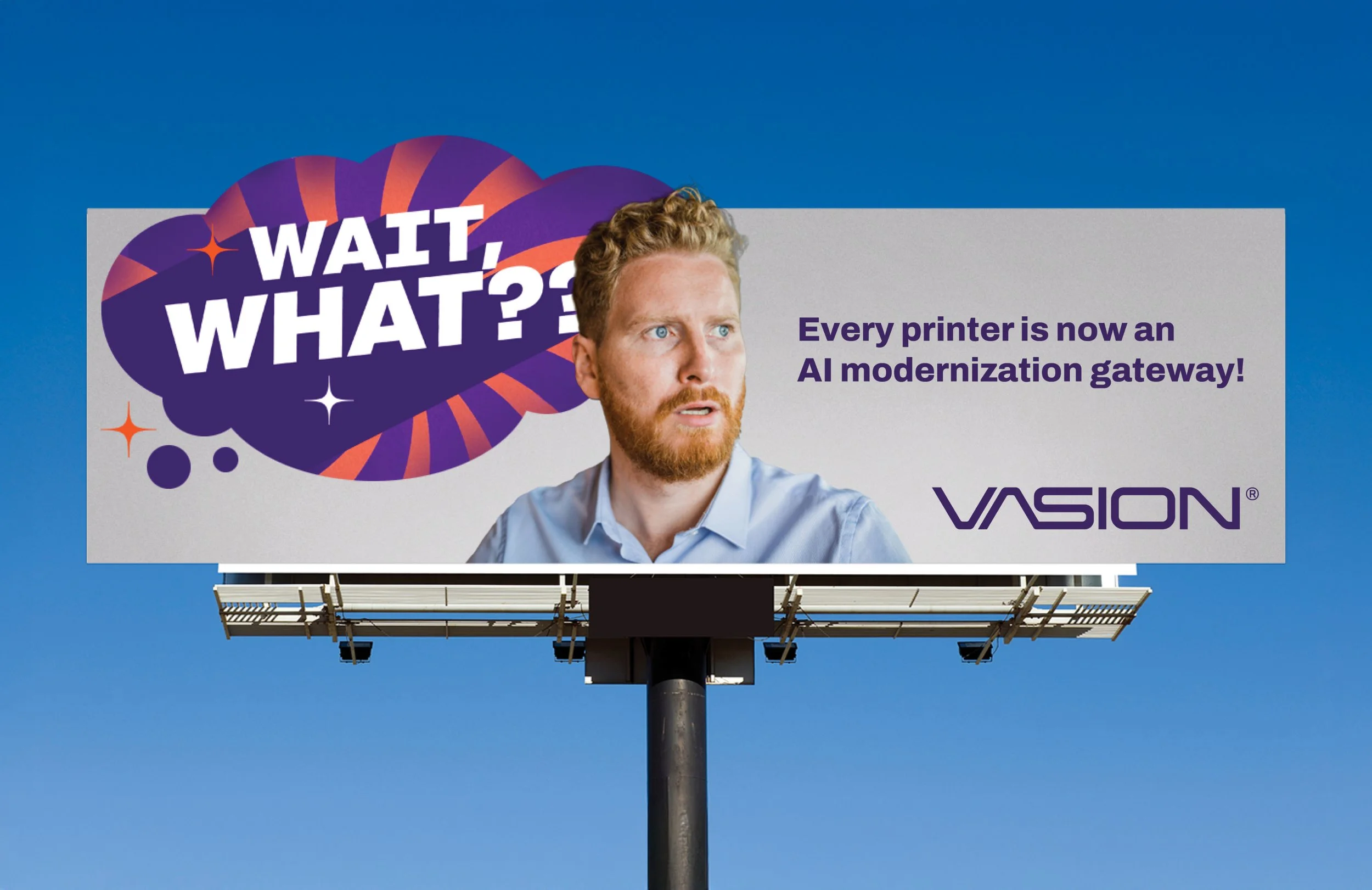 Billboard with a man with red hair and beard looking to the side, text saying 'Wait, What??' in purple and white, and additional purple text about printers being AI modernization gateways, with a blue sky background.