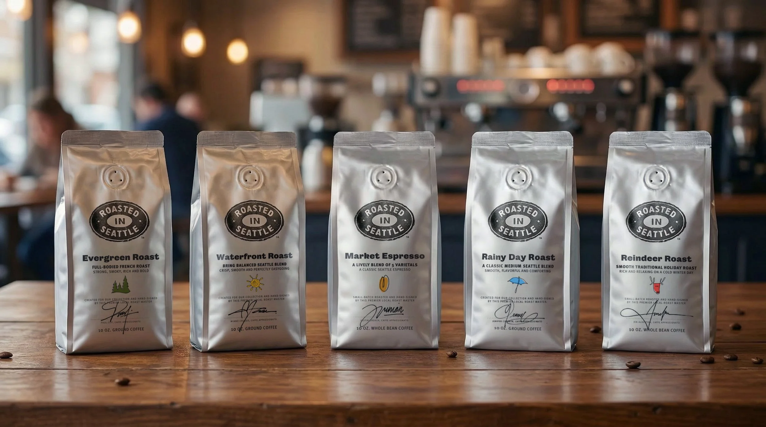Five bags of coffee on a wooden table in a coffee shop, labeled Evergreen Roast, Waterfront Roast, Market Espresso, Rainy Day Roast, and Reindeer Roast, with a blurred background of customers and coffee machines.