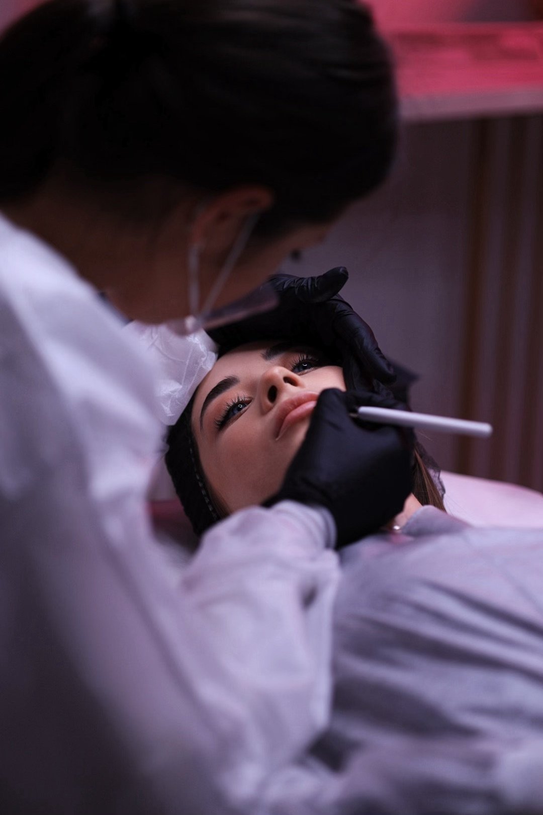 Woman receiving brow treatment from technician in gloves and lab coat