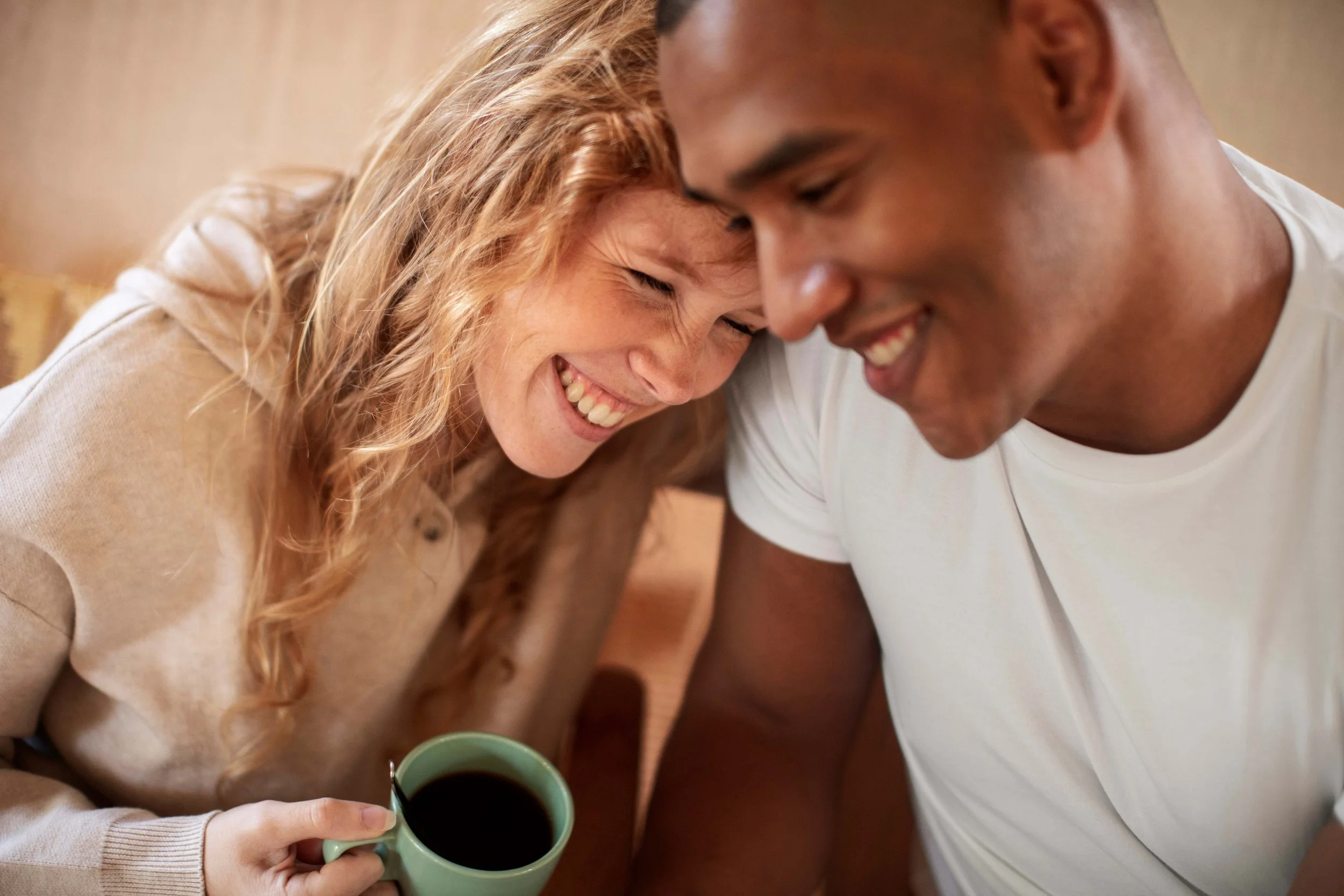 A couple sits close together on a railing, facing a lake with mountains and supporting each other.