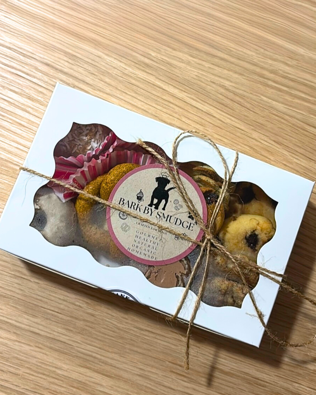 Assorted dog treat box with a variety of fun-shaped, all-natural treats including mini cupcakes, carob cookies, doughnuts, and heart-shaped biscuits