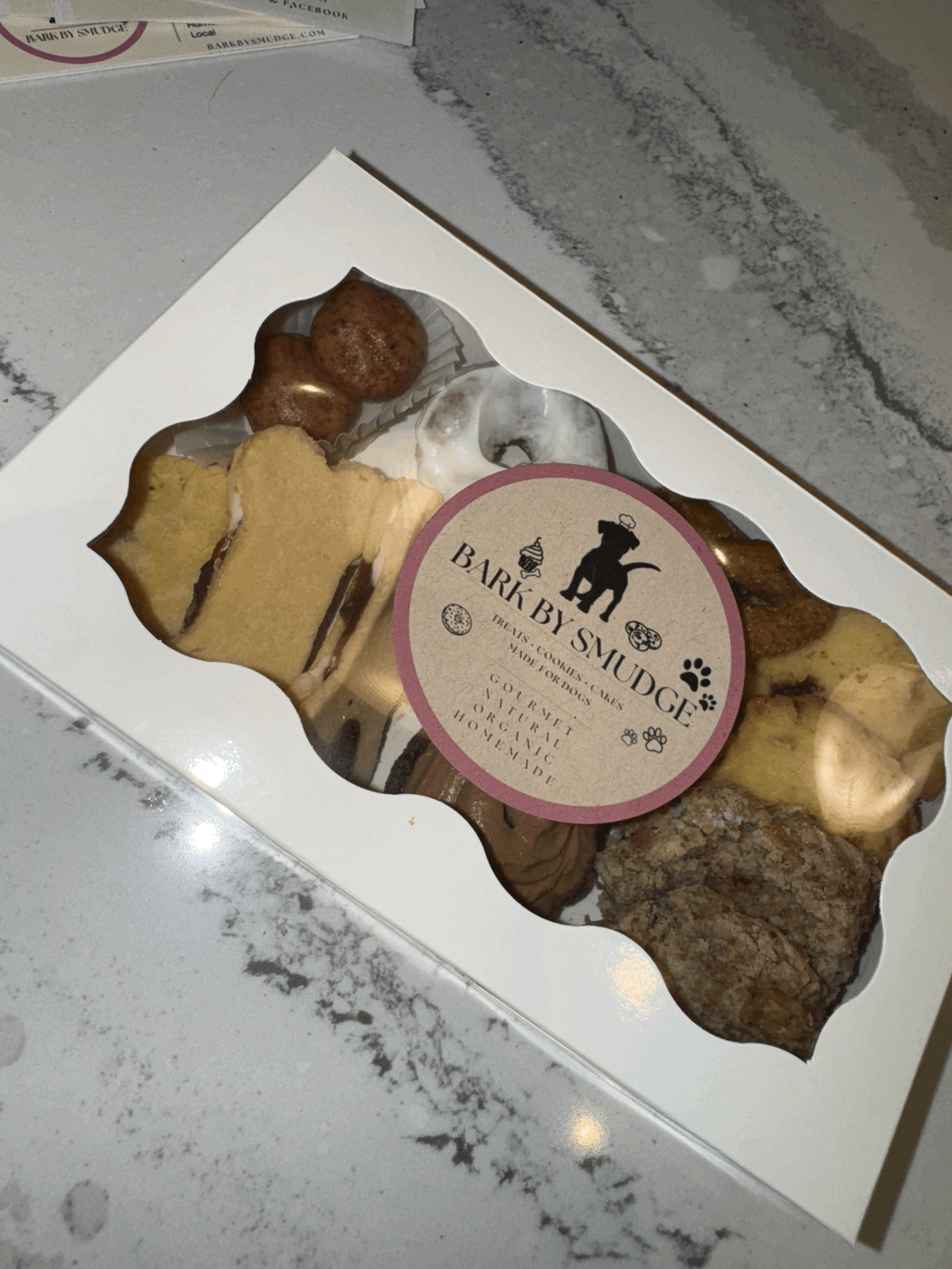 Assorted dog treat box with a variety of fun-shaped, all-natural treats including mini cupcakes, carob cookies, doughnuts, and heart-shaped biscuits