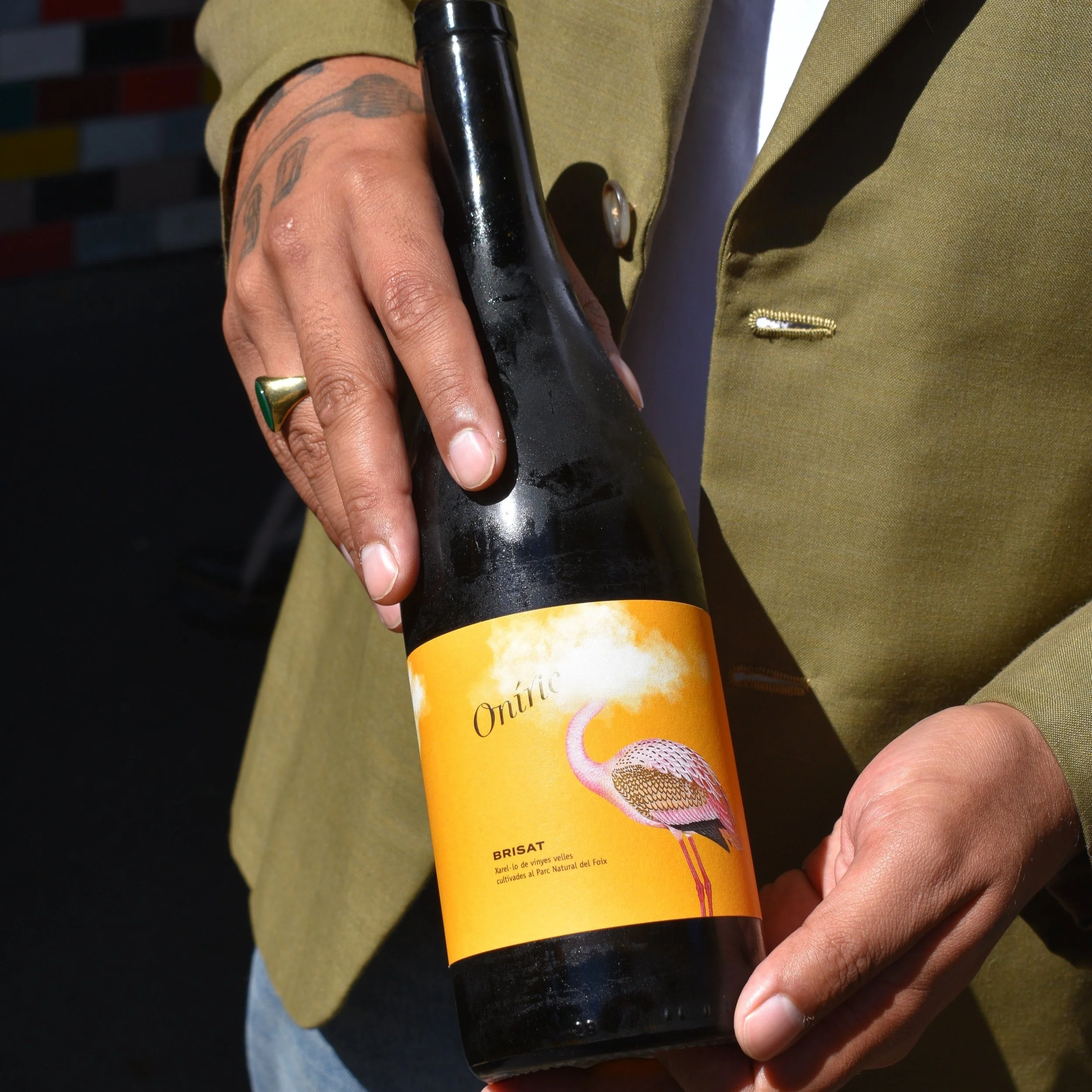 A person holding a black bottle with a yellow label featuring a pink flamingo and some text.