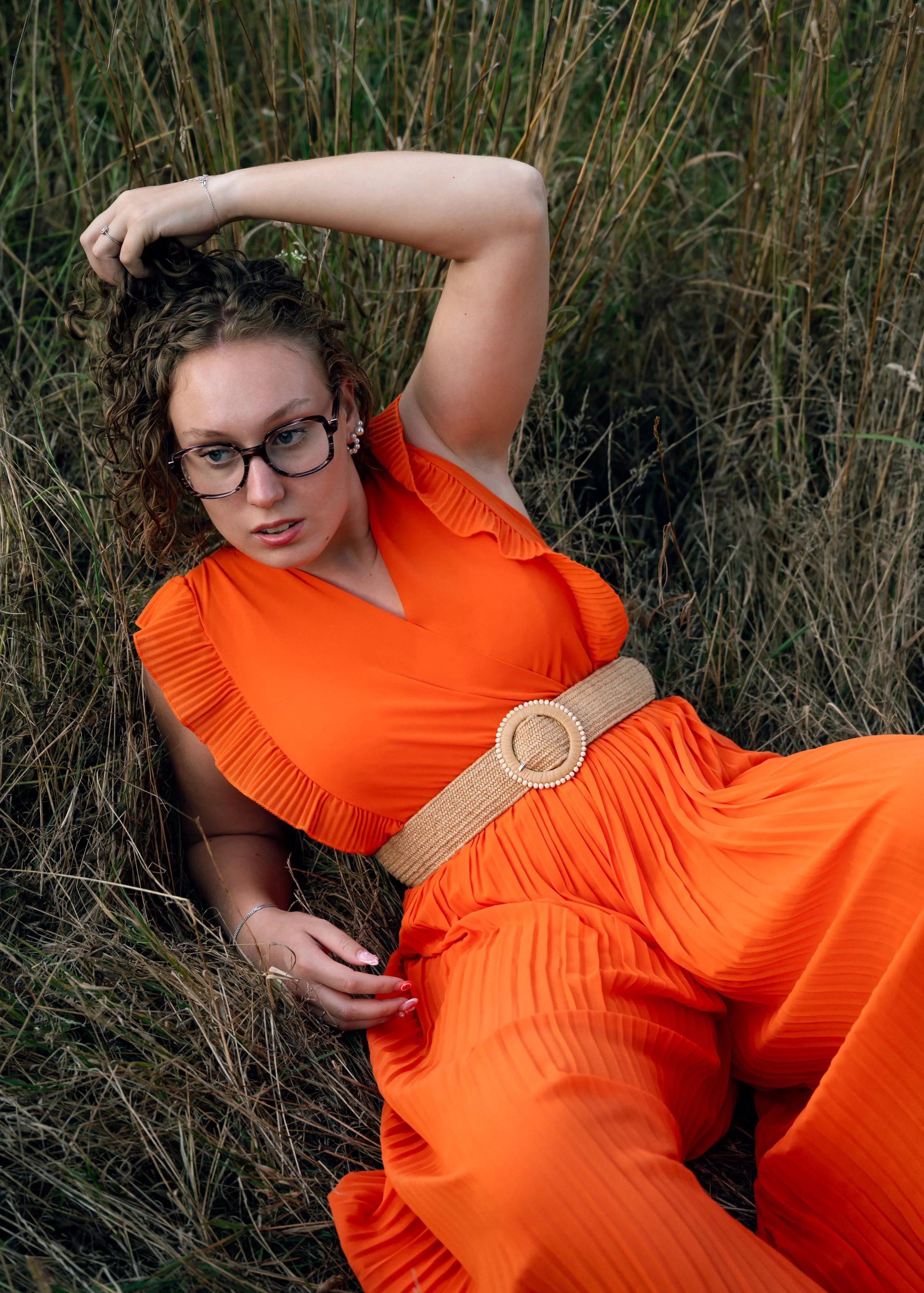 Photographie mode éditoriale dans un champ. Mise en lumière d'une robe orange contrastant avec la couleur verte du champ. La lumière dorée fait ressortir le modèle.