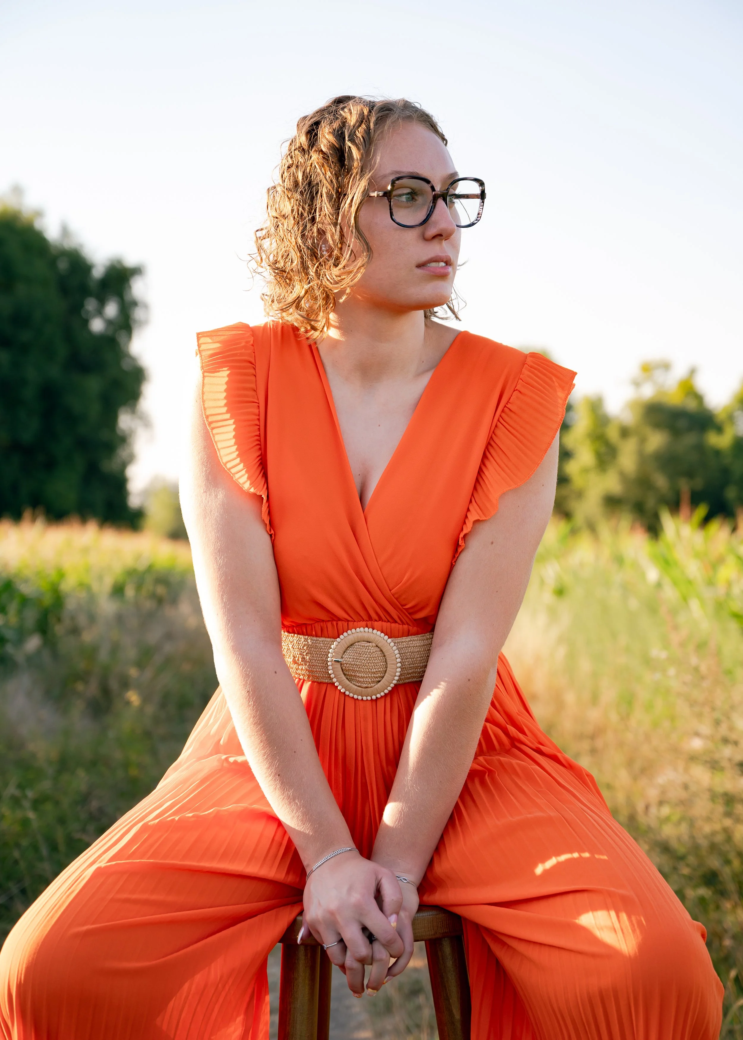 Photographie mode éditoriale dans un champ. Mise en lumière d'une robe orange contrastant avec la couleur verte du champ. La lumière dorée fait ressortir le modèle.