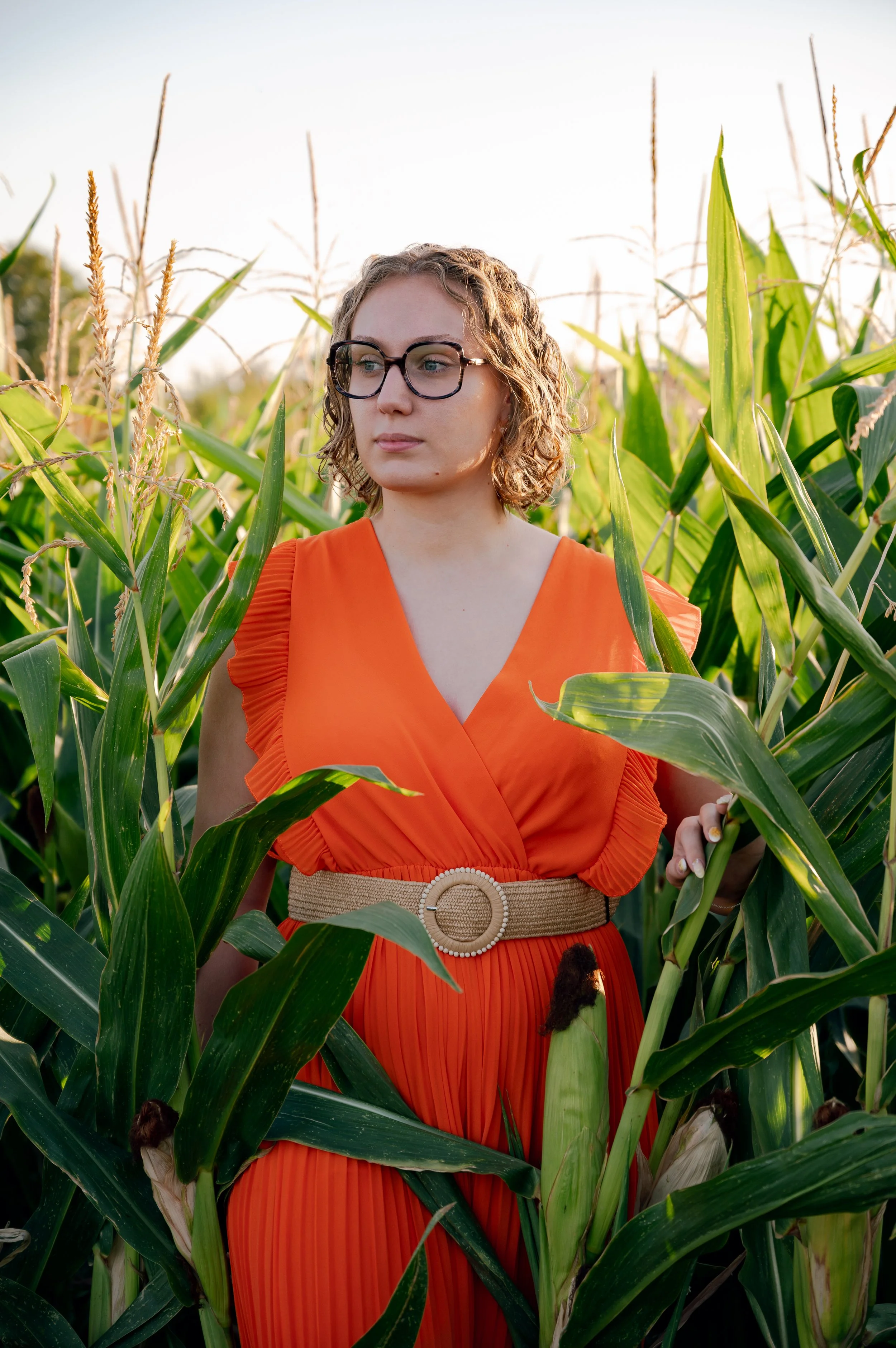 Photographie mode éditoriale dans un champ. Mise en lumière d'une robe orange contrastant avec la couleur verte du champ. La lumière dorée fait ressortir le modèle.