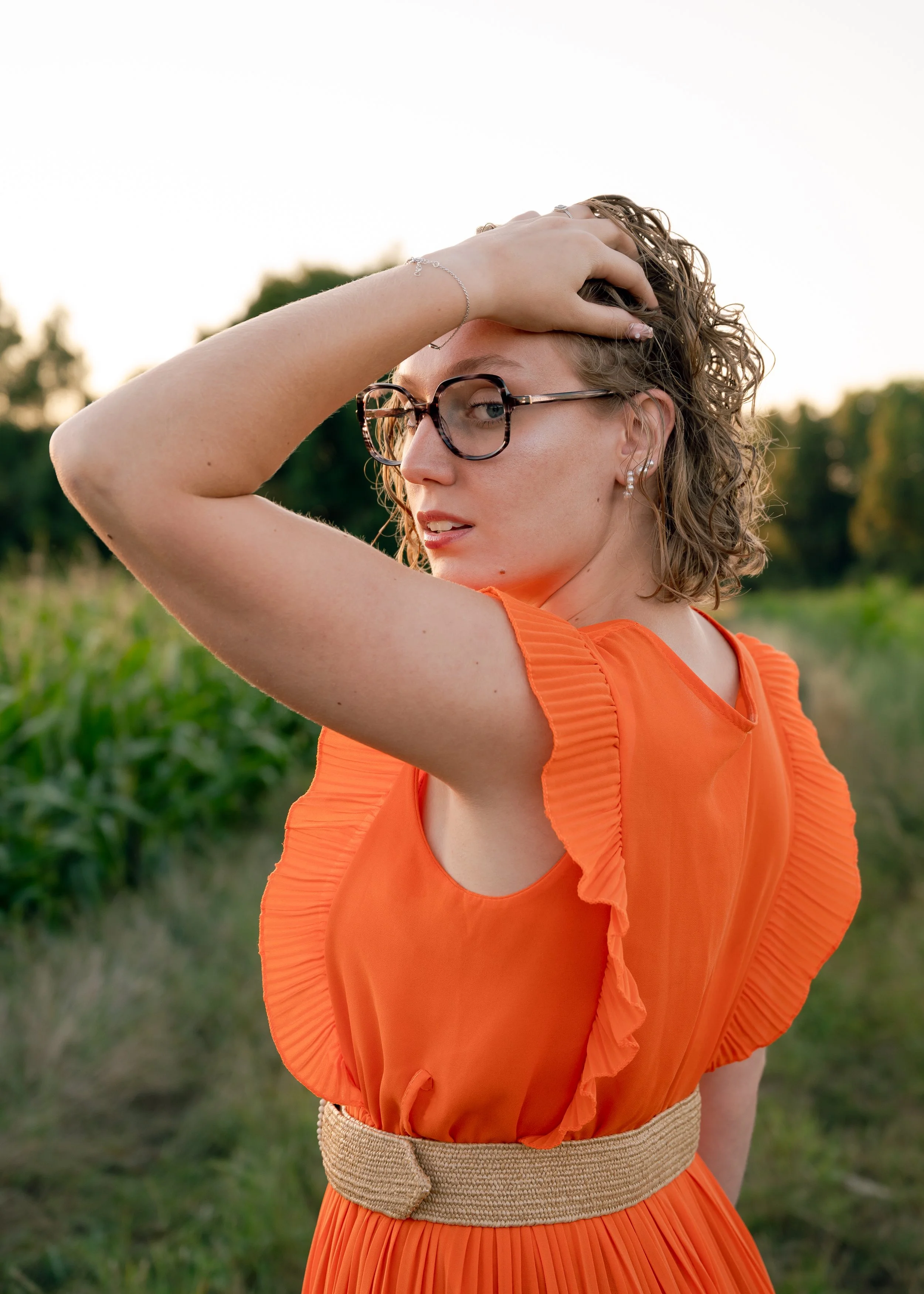 Photographie mode éditoriale dans un champ. Mise en lumière d'une robe orange contrastant avec la couleur verte du champ. La lumière dorée fait ressortir le modèle.