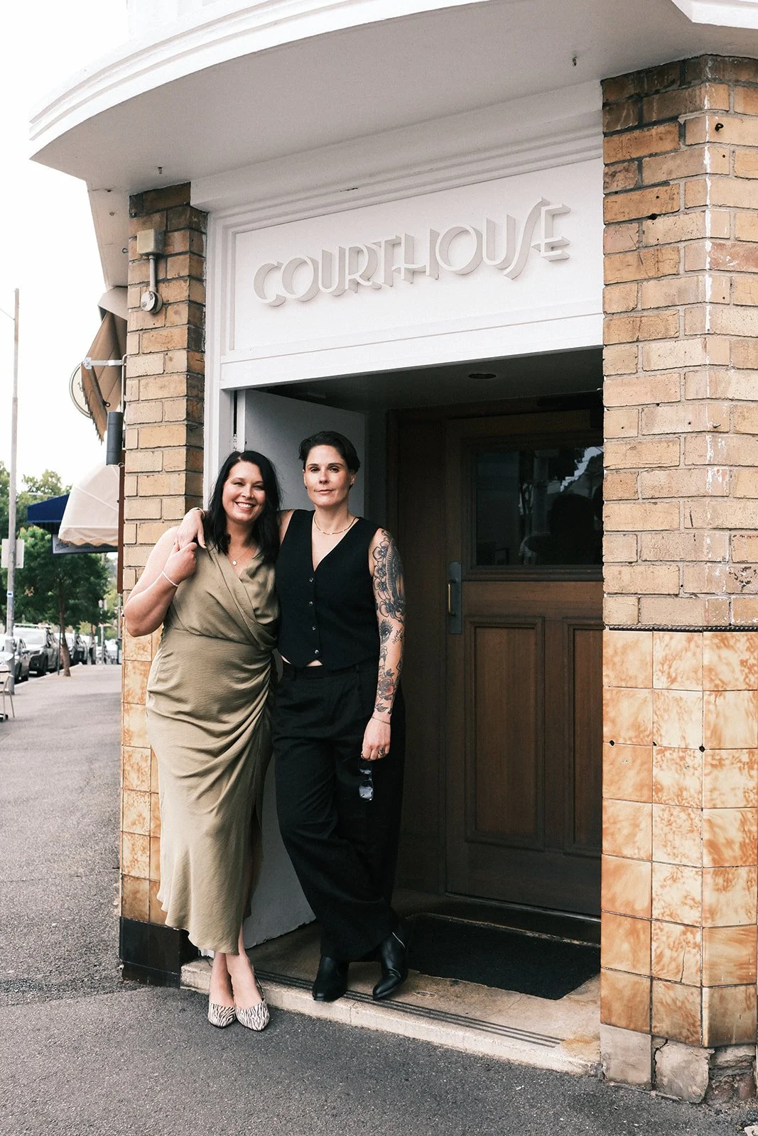 A couple at their engagement party at the Courthouse Hotel in Melbourne. They are standing together, with their arms around each other.