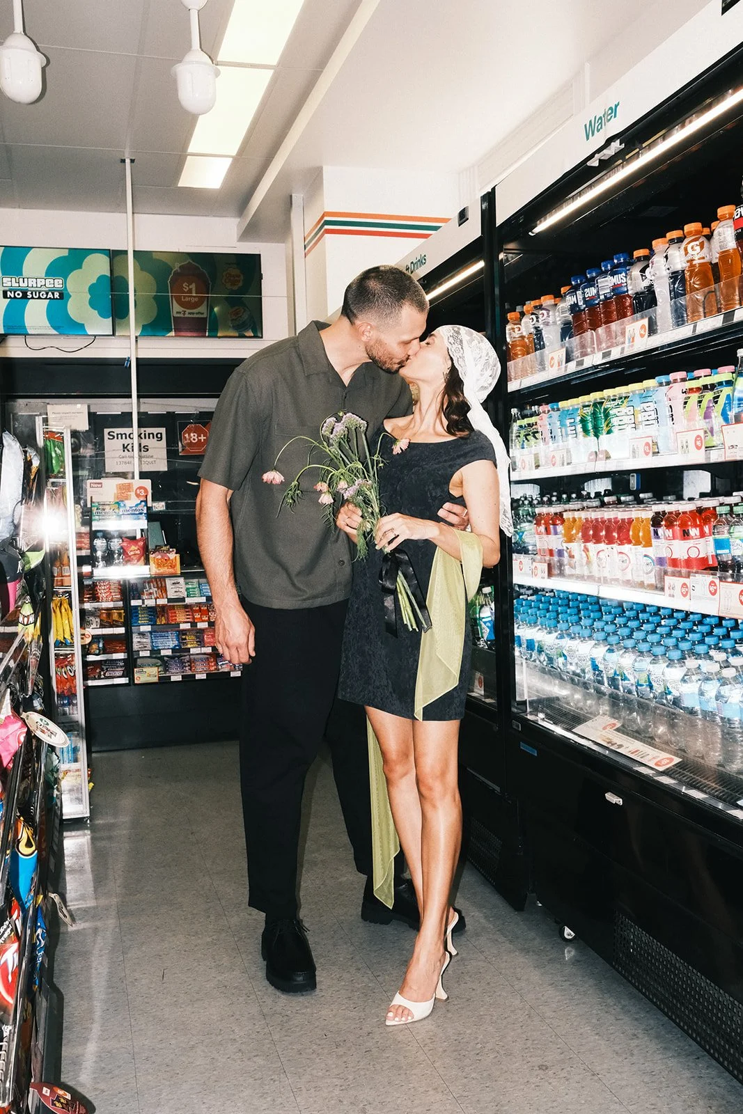 A couple kissing while on their engagement shoot. They are standing in the aisle of a 7-eleven.