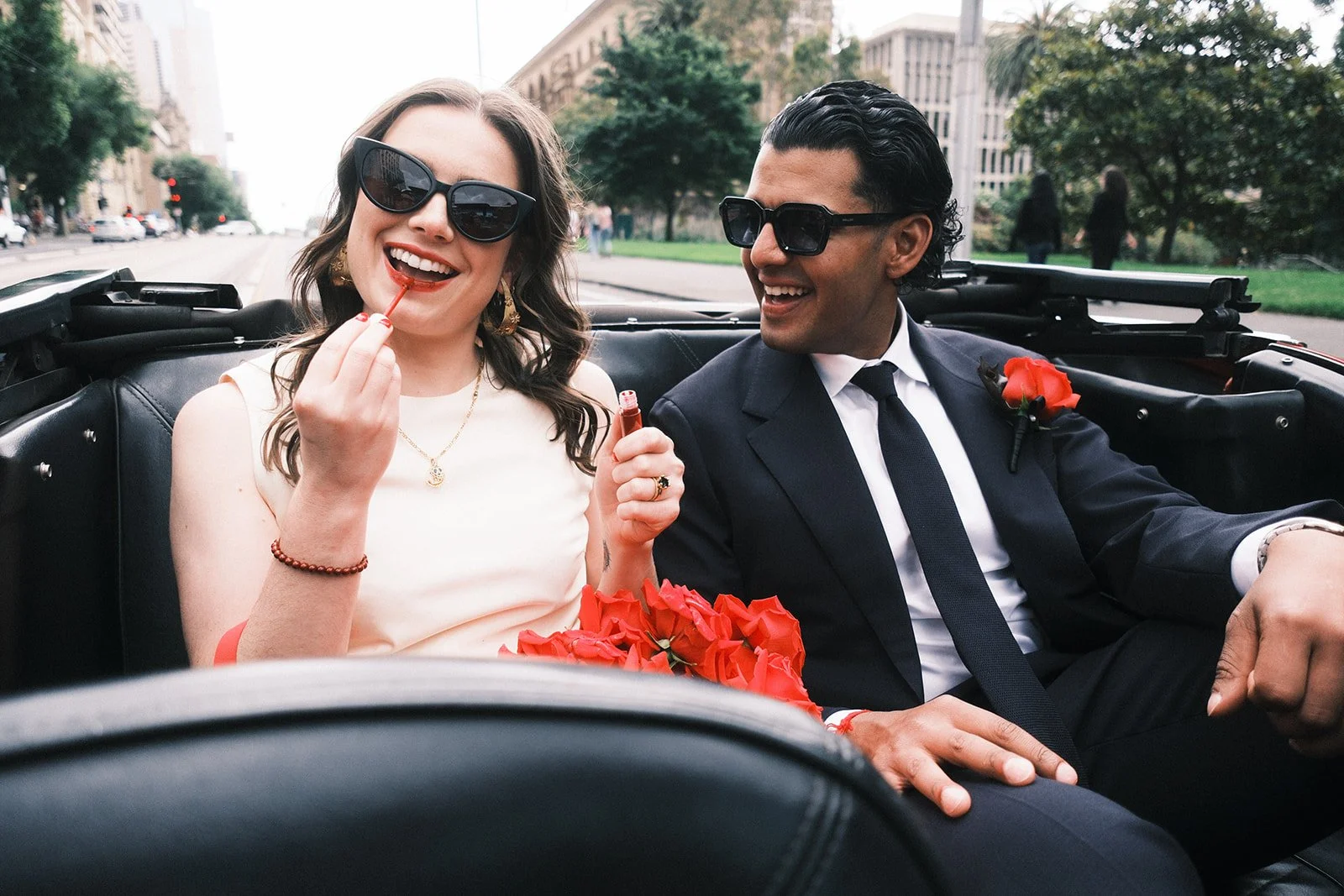 a bride and groom riding in their hire car after getting married at the Victorian Marriage Regsitry in Melbourne. The bride is applying lipstick and smiling.