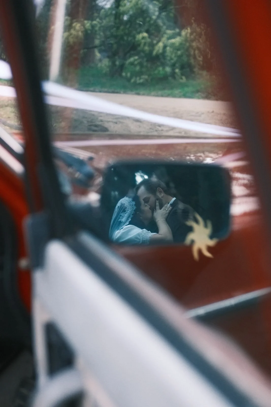 A bride and groom kissing, captured through the mirror of their car in Red Hill