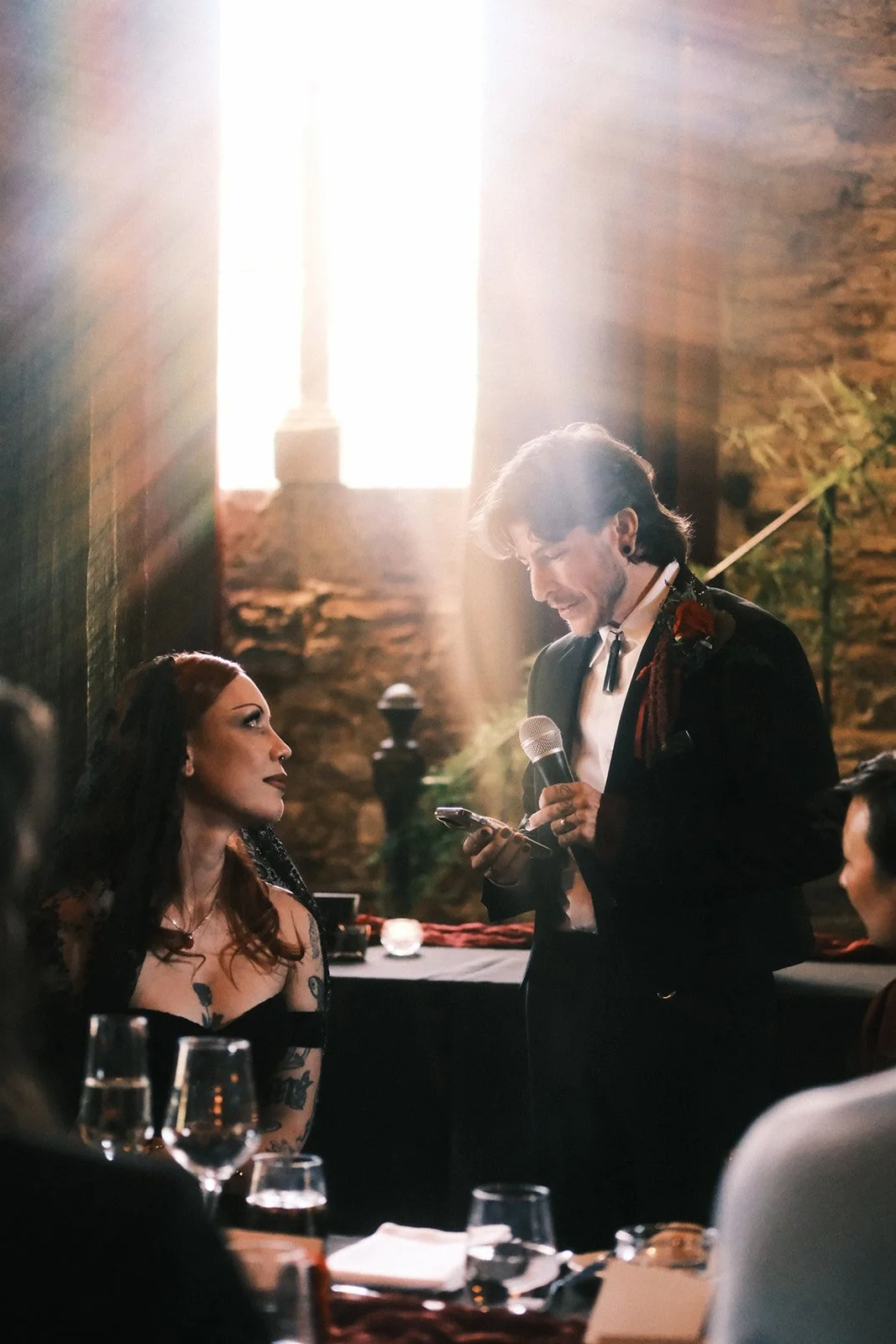 A bride and groom during speeches at their wedding at Montsalvat in the Yarra Valley. There's a beam of light coming from the window behind them.