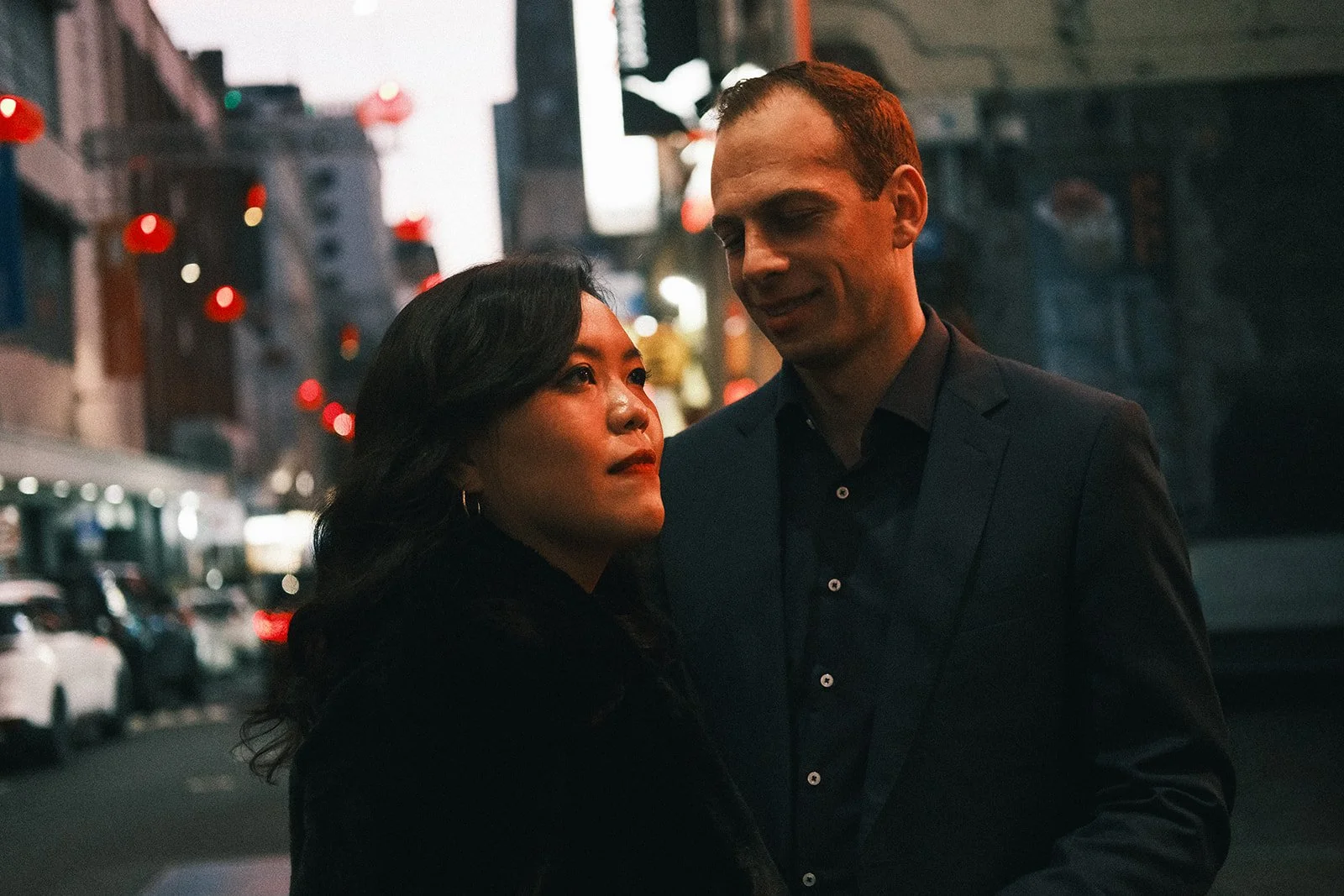 A bride and groom at their engagement shoot in Chinatown in Melbourne. The groom is looking at his wife, and their faces glow red from the neon lights in the street.