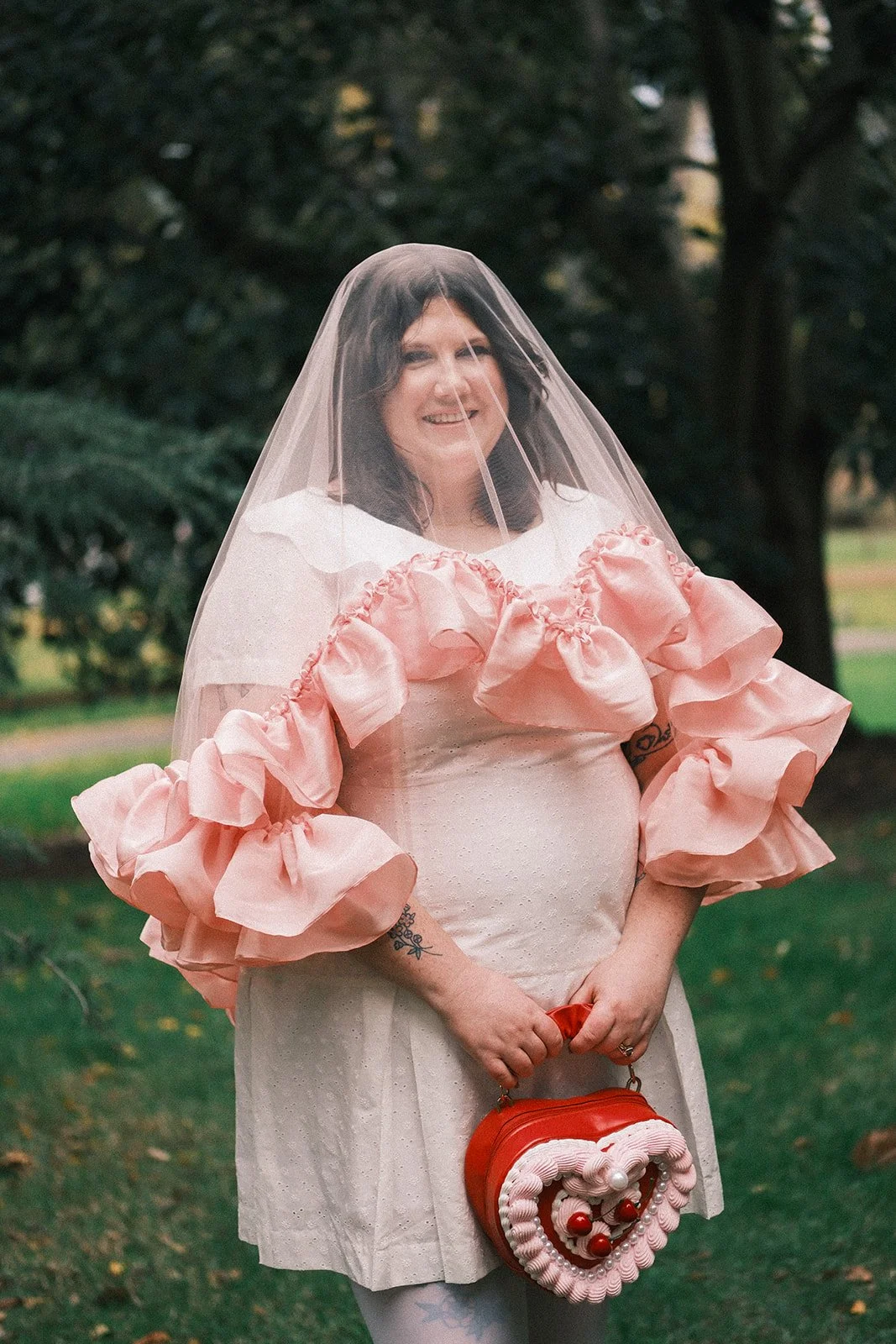 A bride after her elopement in the Treasury Gardens in Melbourne. She's wearing a Madison Chamberlain veil over her face, and holding a bag shaped like a cake.