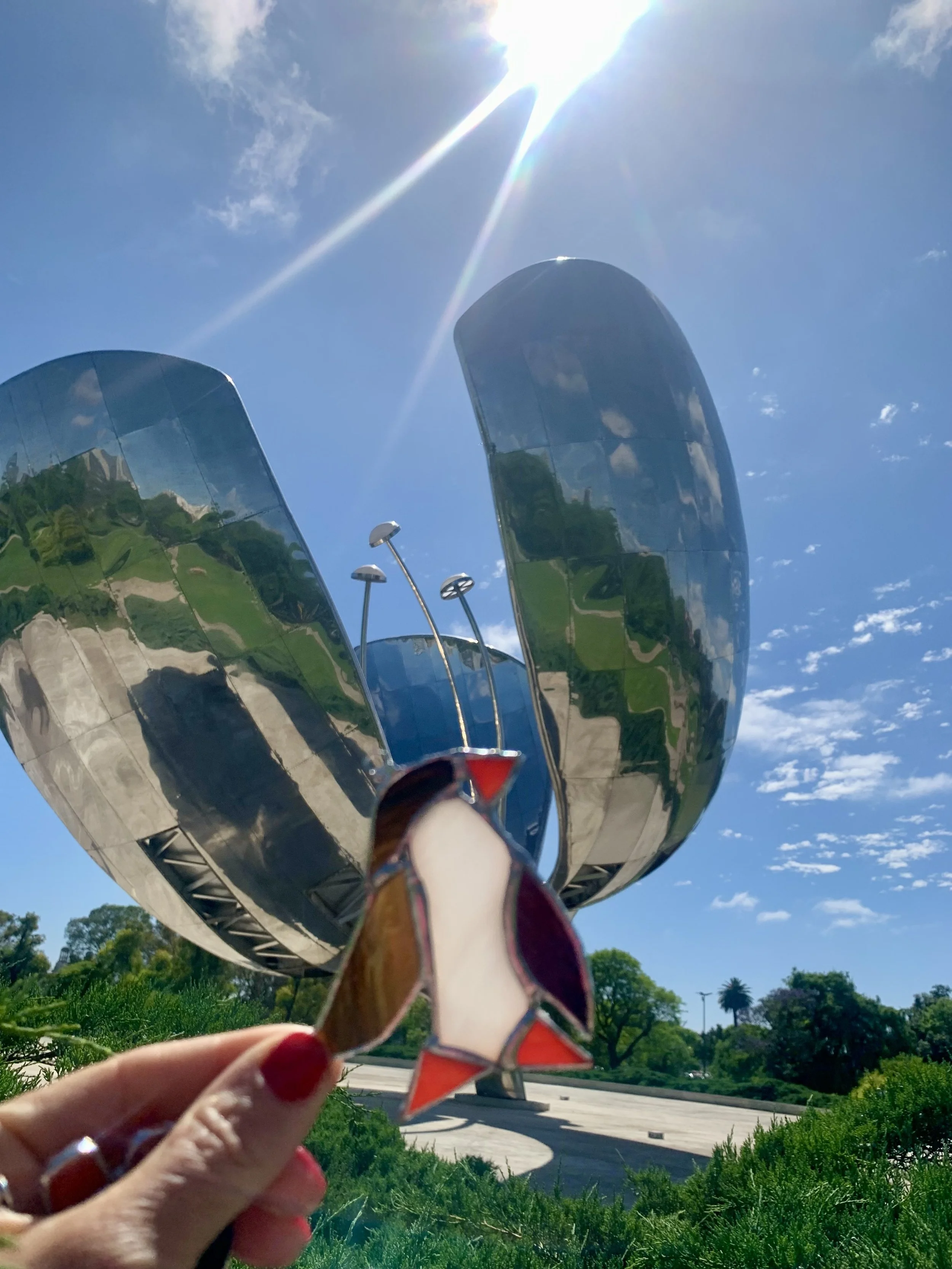 Tiffany stained glass penguin in front of the BMW Museum building, with bright sunlight and a clear blue sky in the background.