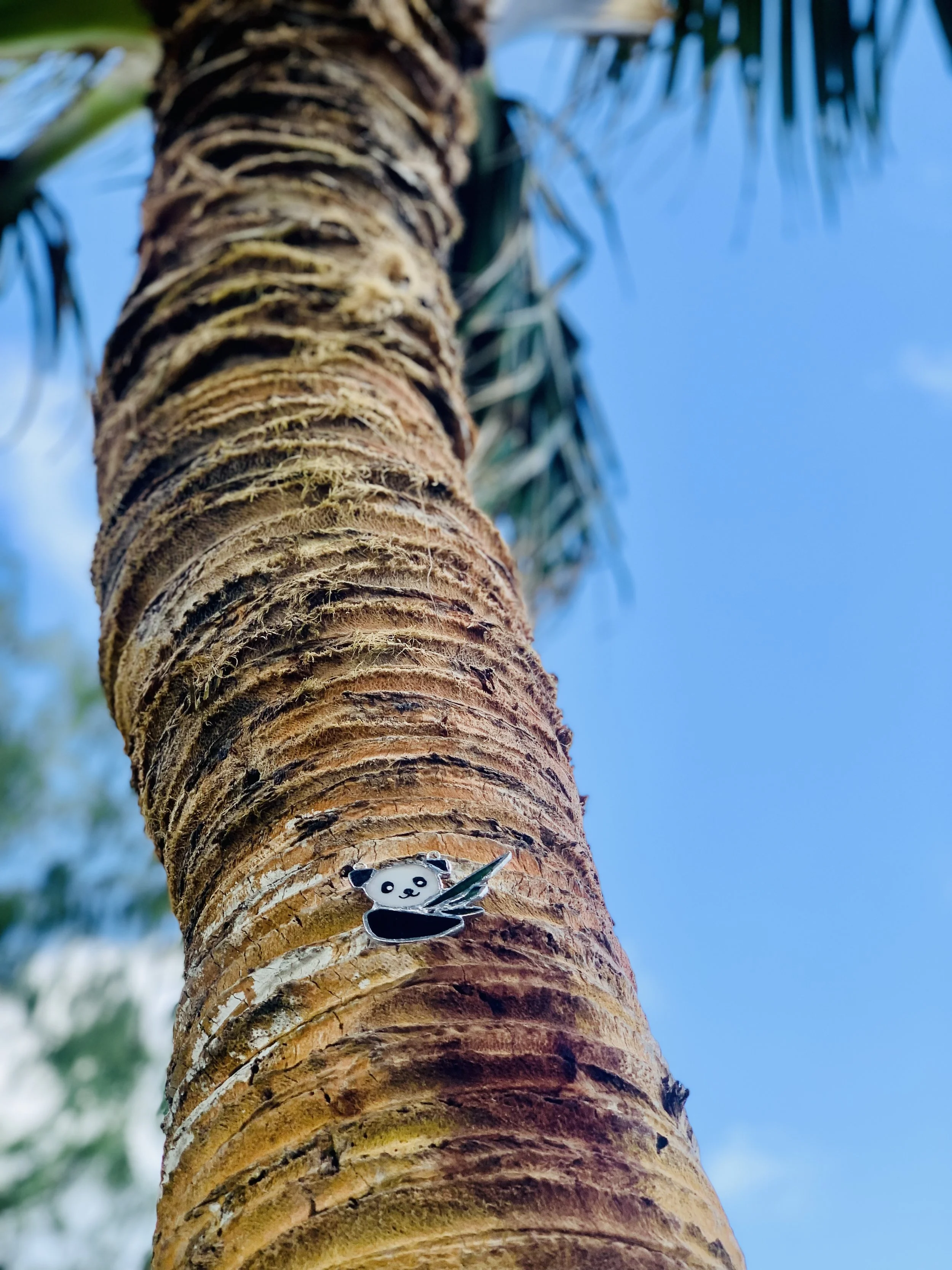 Close-up of a palm tree trunk with a panda stained glass, on a beach in Hawaii, with green fronds and blue sky in the background.