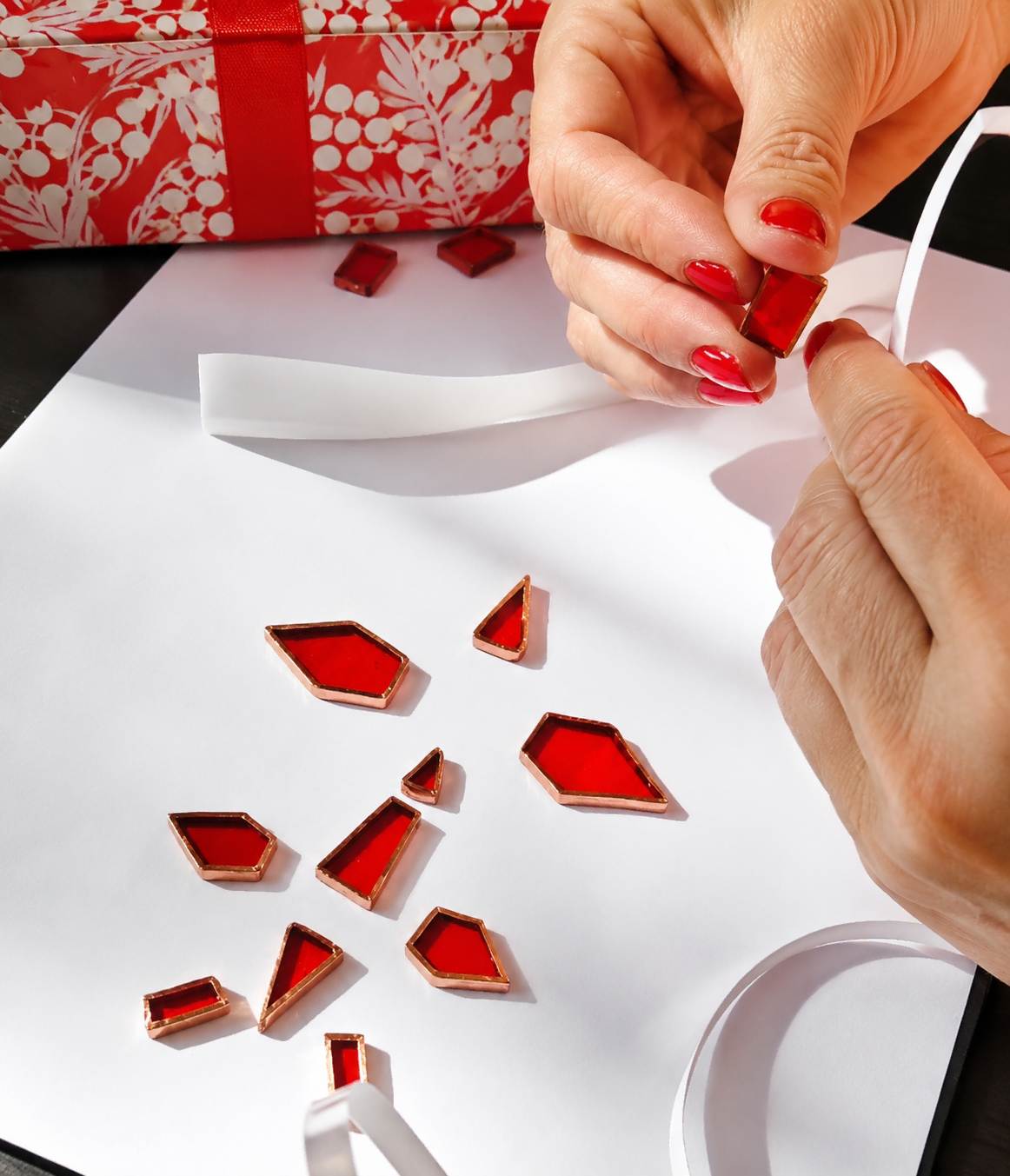 Maria Avram applying copper foil to hand-cut red stained glass pieces using the Tiffany method.
